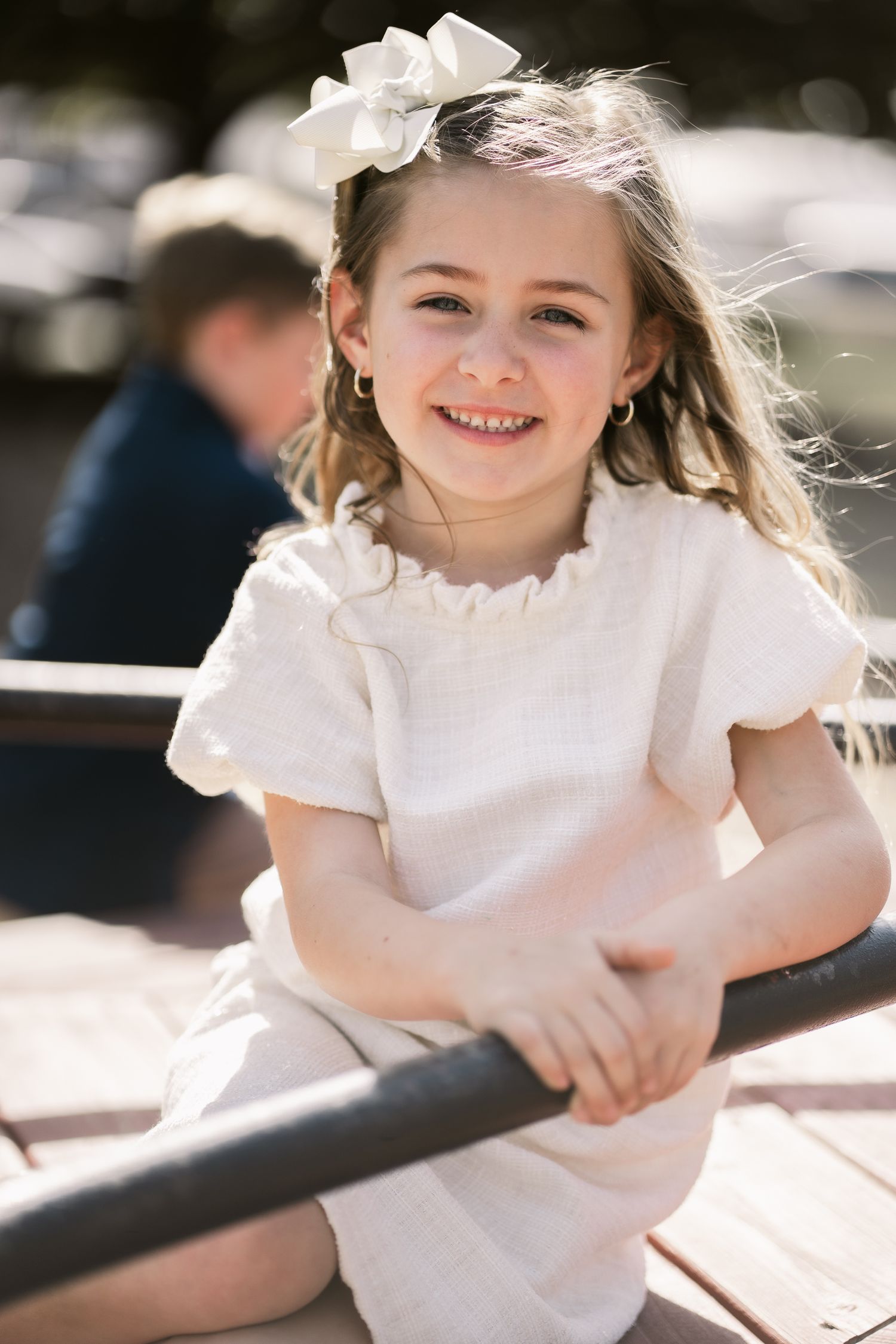 Young girl in white dress smiling and laughing in outdoor sunlit setting.