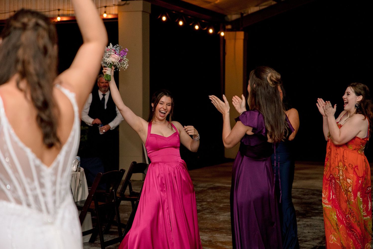 Excited bridesmaid in pink gown celebrates catching the bouquet toss at a wedding reception.