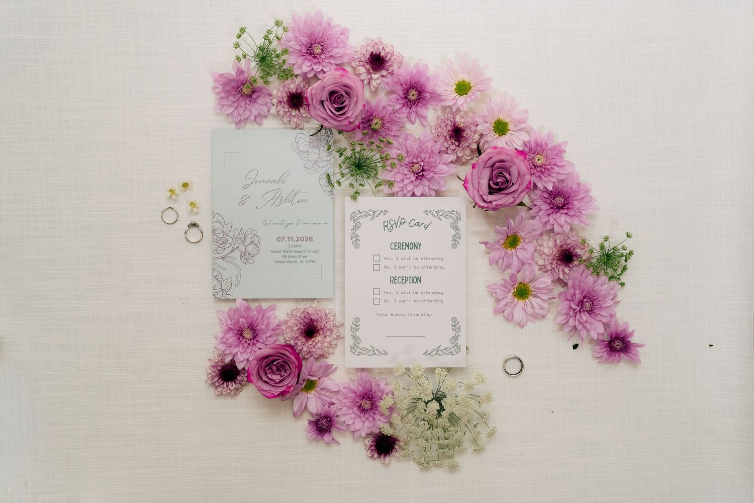 Elegant wedding invitation suite surrounded by pink roses and purple daisy flowers on a white background.