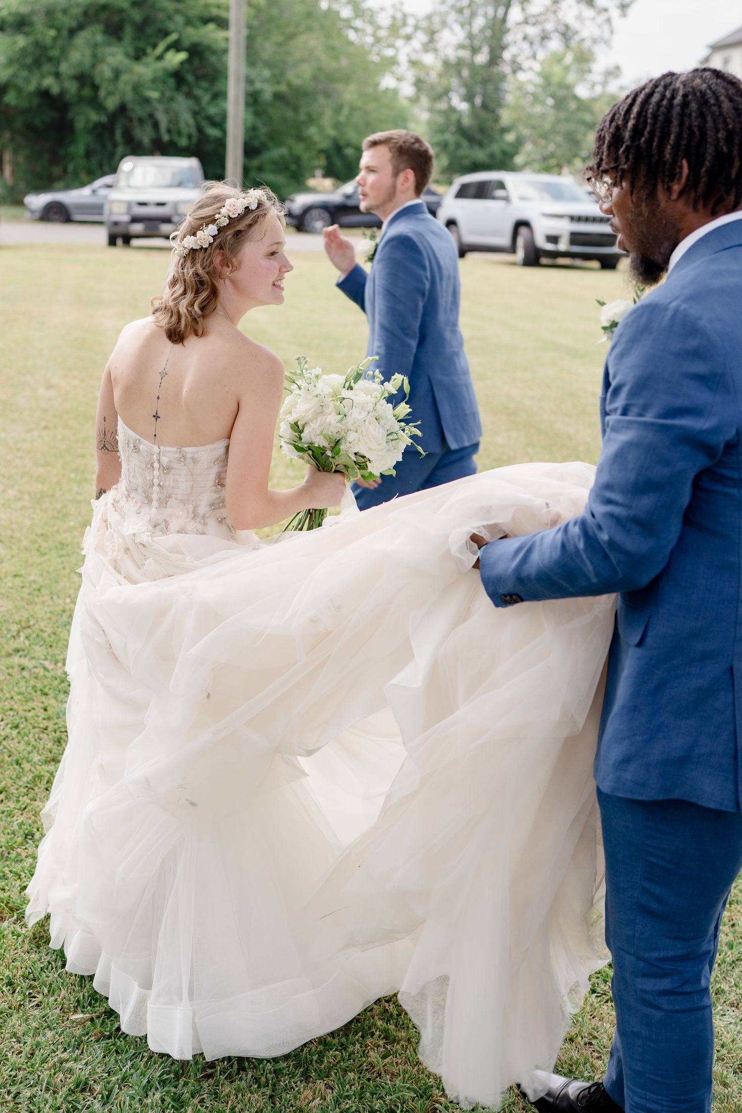 A couple in wedding attire twirls together on a grassy lawn, with the bride's white dress flowing elegantly in motion.