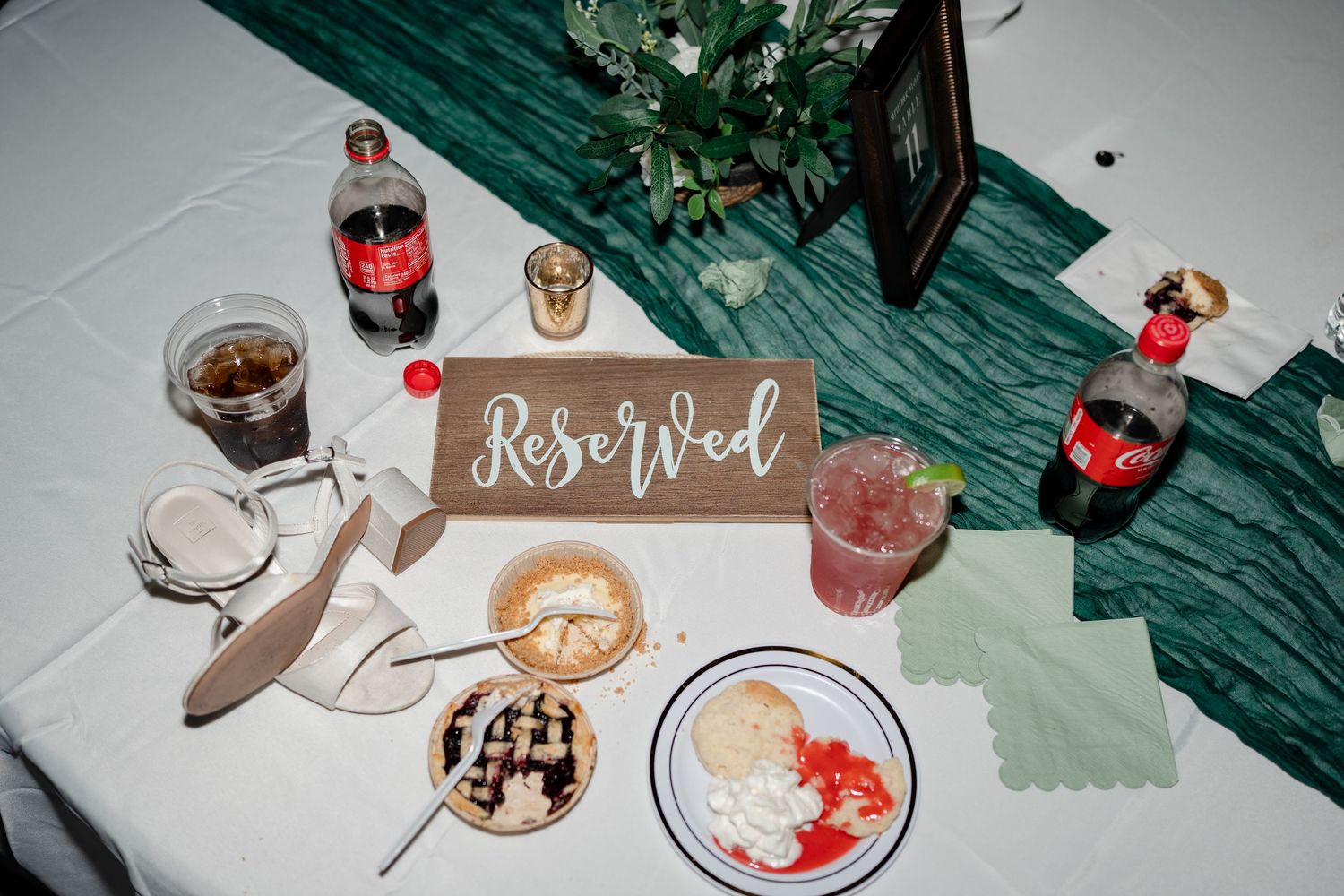 Wedding reception tables decorated with drinks and place settings on a dark green tablecloth.