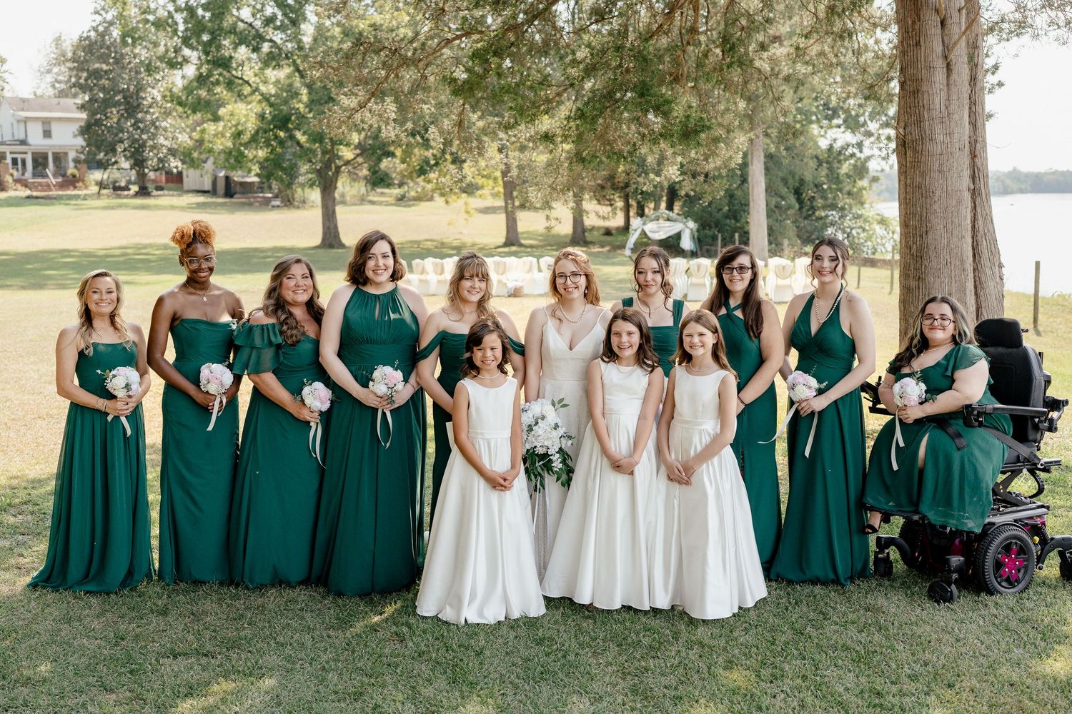 Wedding party arranged in a casual seated pose on grass with bridesmaids in emerald dresses and white gowns.