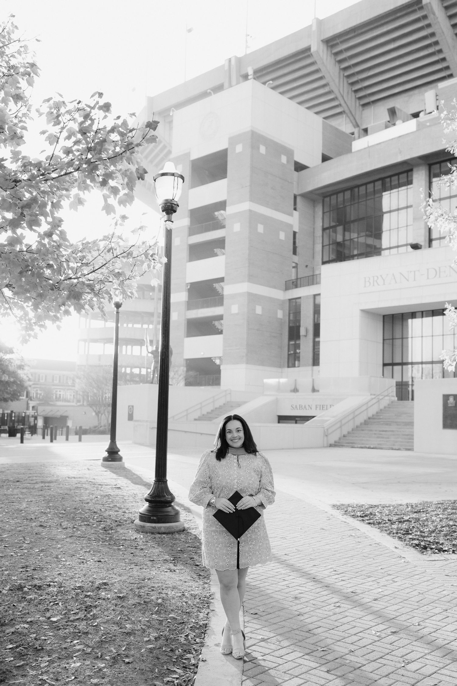 A graduation photoshoot in front of a modern university building with a lamp post on a brick pathway.