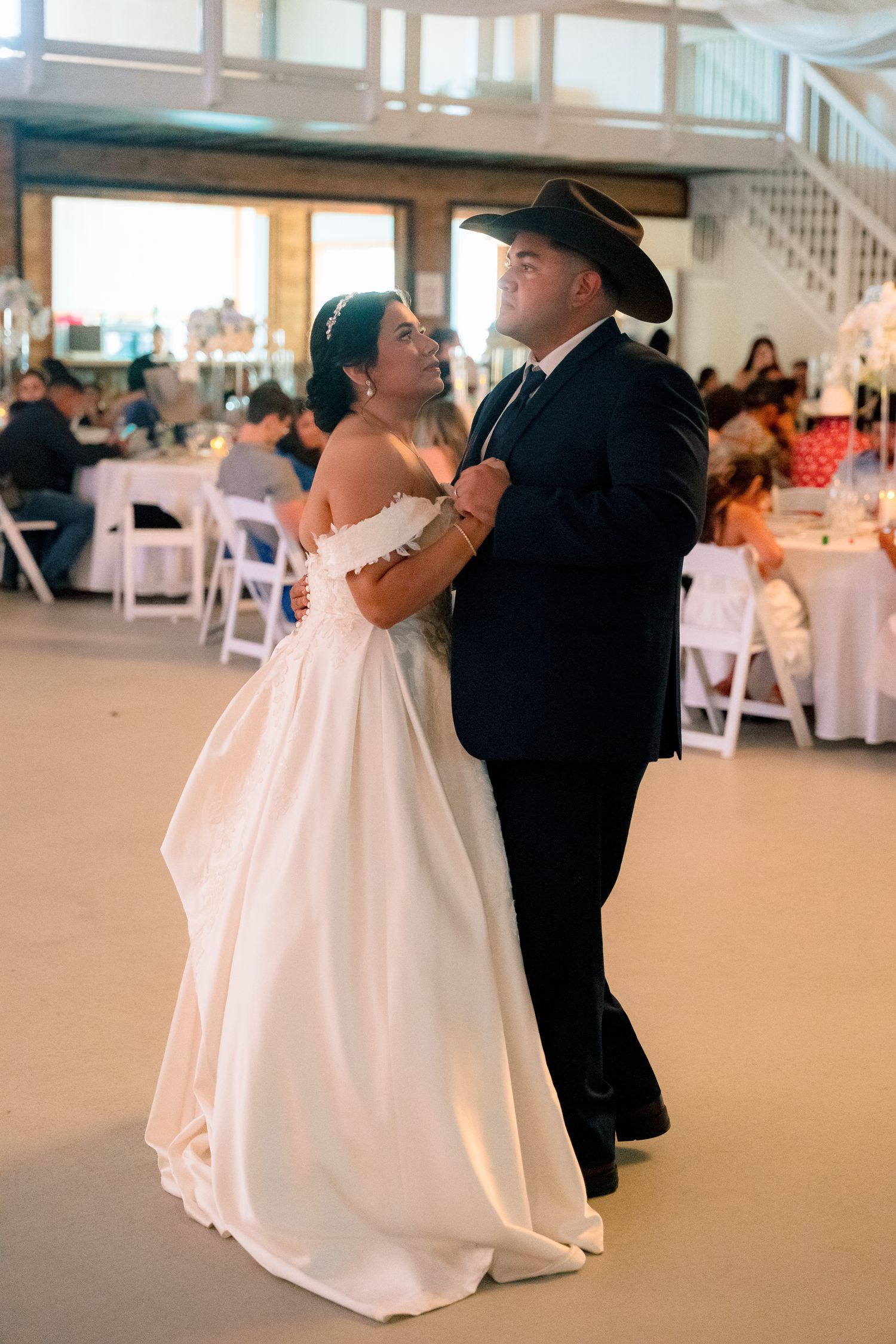A couple in wedding attire dance together at their reception in a spacious venue with white decor.