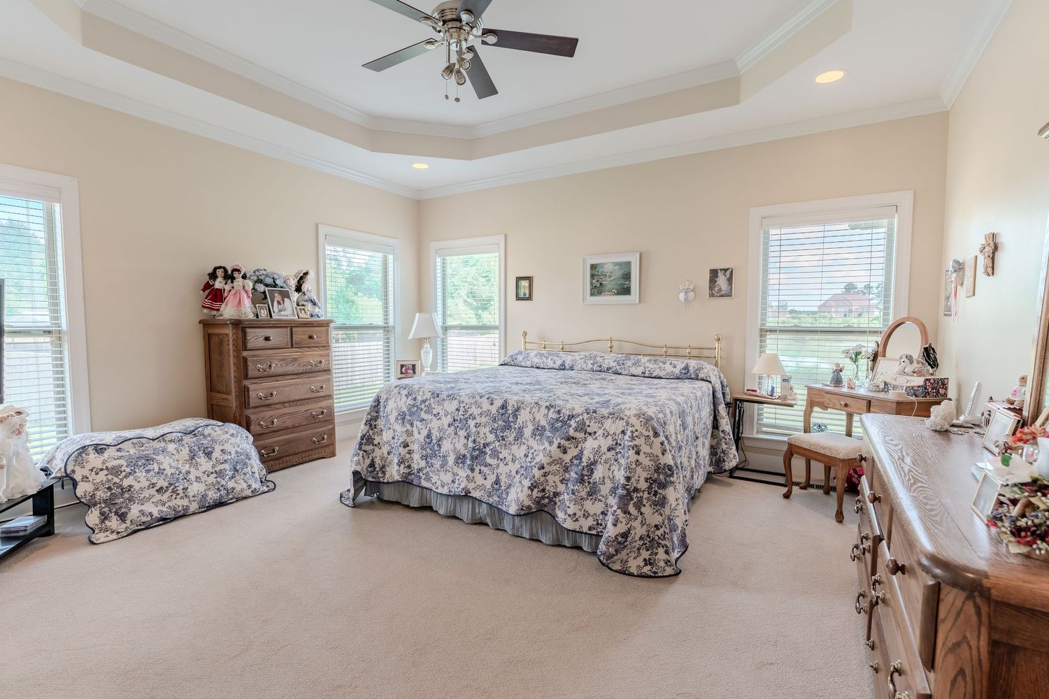 Spacious bedroom with tray ceiling, floral bedding, and large windows letting in natural light.