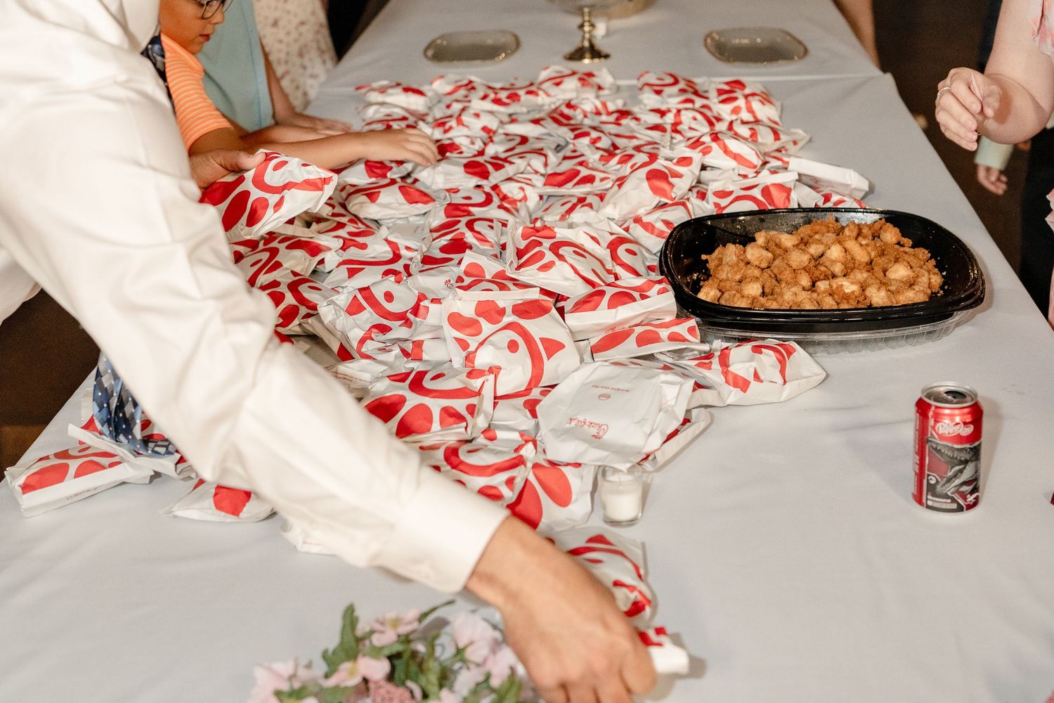 Hands reach for red and white peppermint candies scattered across a white tablecloth at a holiday gathering.