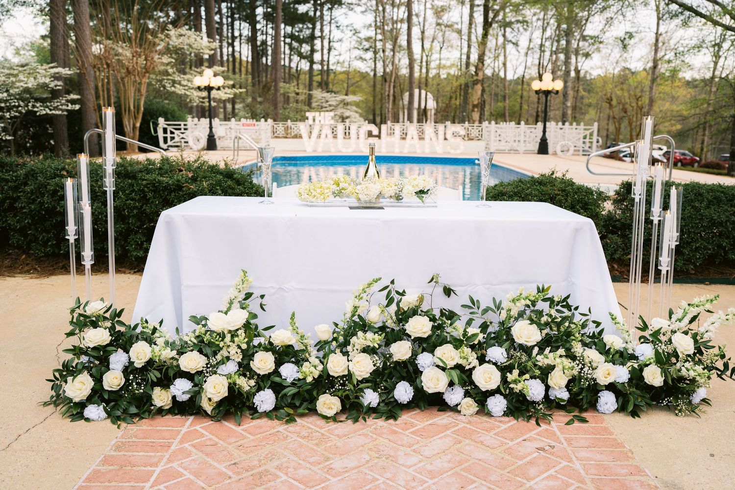 Wedding reception table with lush white floral arrangements and candles overlooking pool.