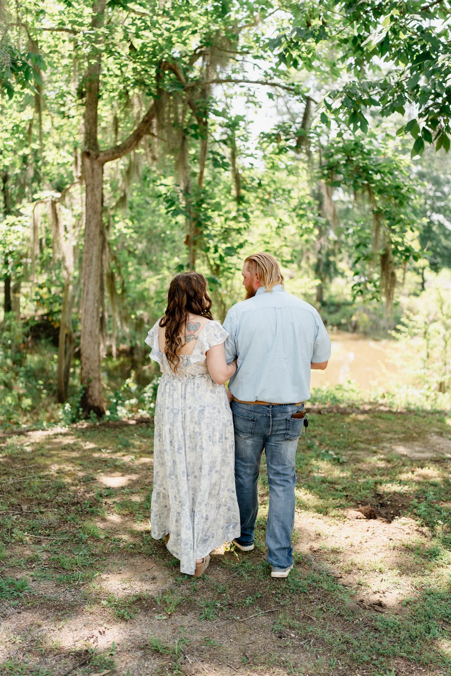 Couple walks hand in hand through wooded area in coordinated outfits.