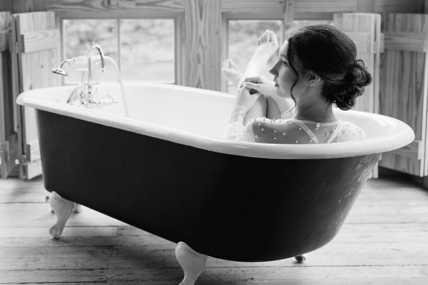 Black and white photo of a bride sitting in a clawfoot bathtub holding her veil.
