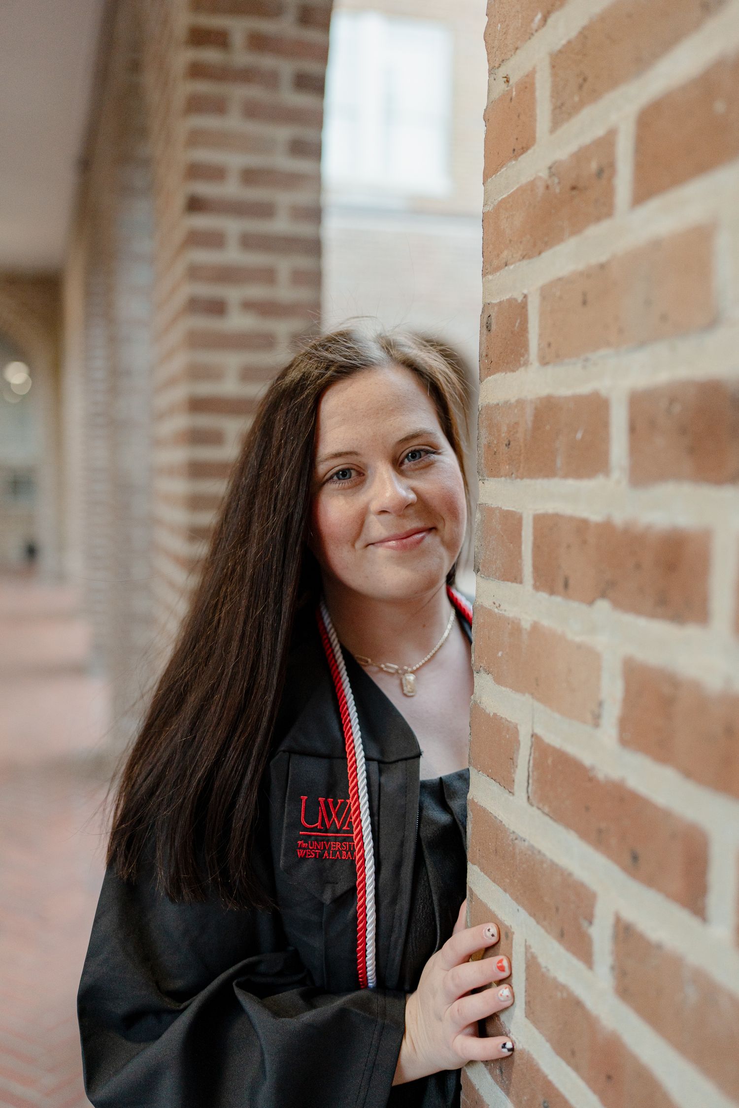 Graduate wearing a black UW graduation gown poses against a brick wall with a warm smile.