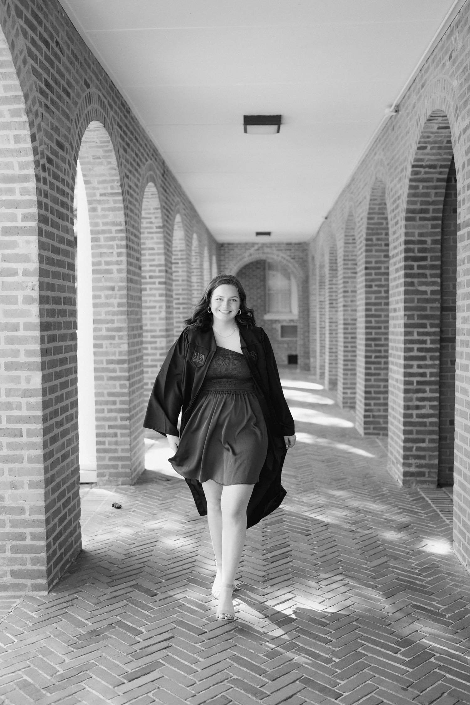 Black and white photo of someone walking through an elegant brick archway corridor with herringbone patterned floor.