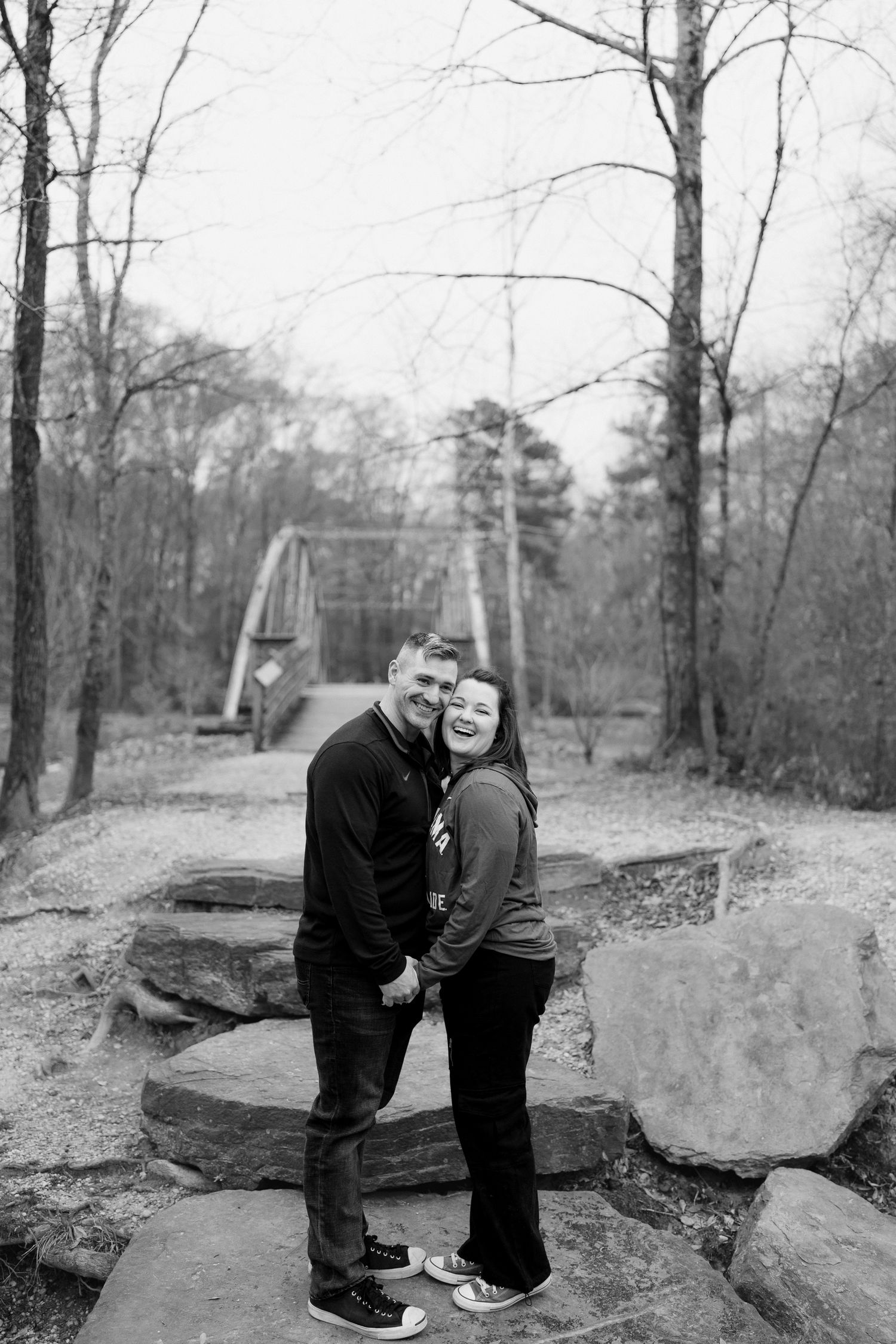 A couple shares a joyful moment together on rocky terrain with a bridge visible in the background.
