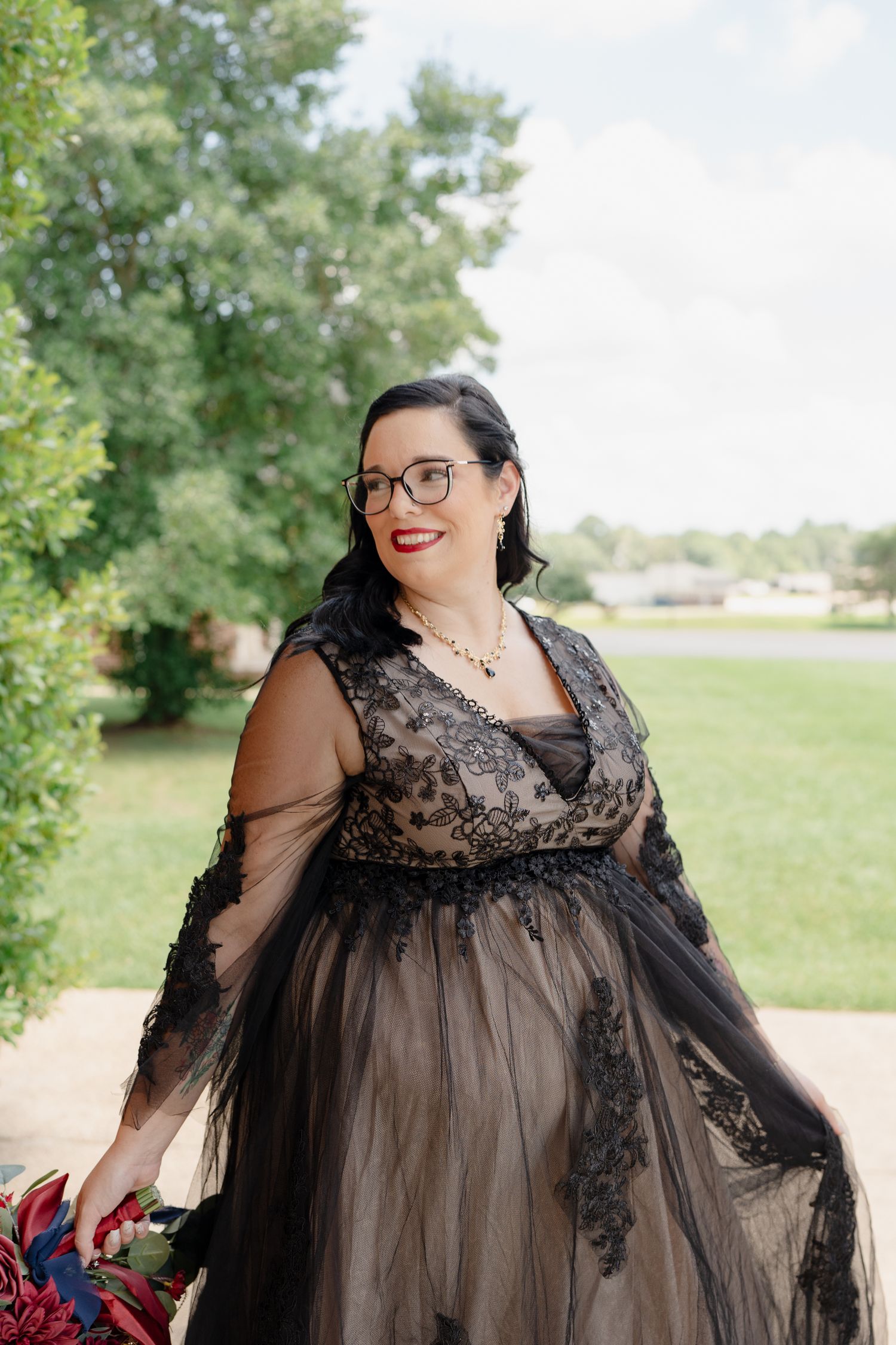 Person in a flowing black lace gown poses outdoors against a natural landscape background.
