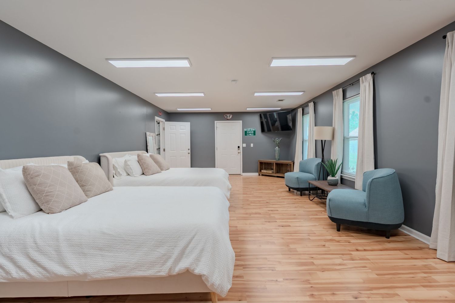 Modern office space with light wood flooring, gray walls, and fluorescent ceiling lights in a long hallway.