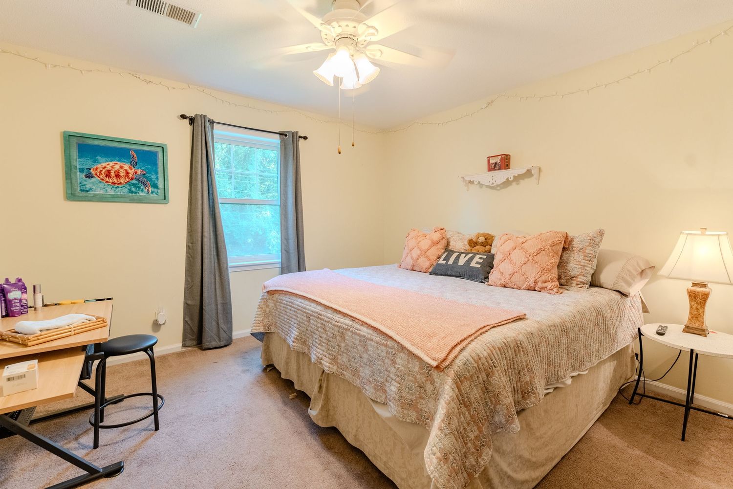Bright bedroom with cream walls, ceiling fan, and multiple beds featuring floral bedspreads in a guest suite layout.