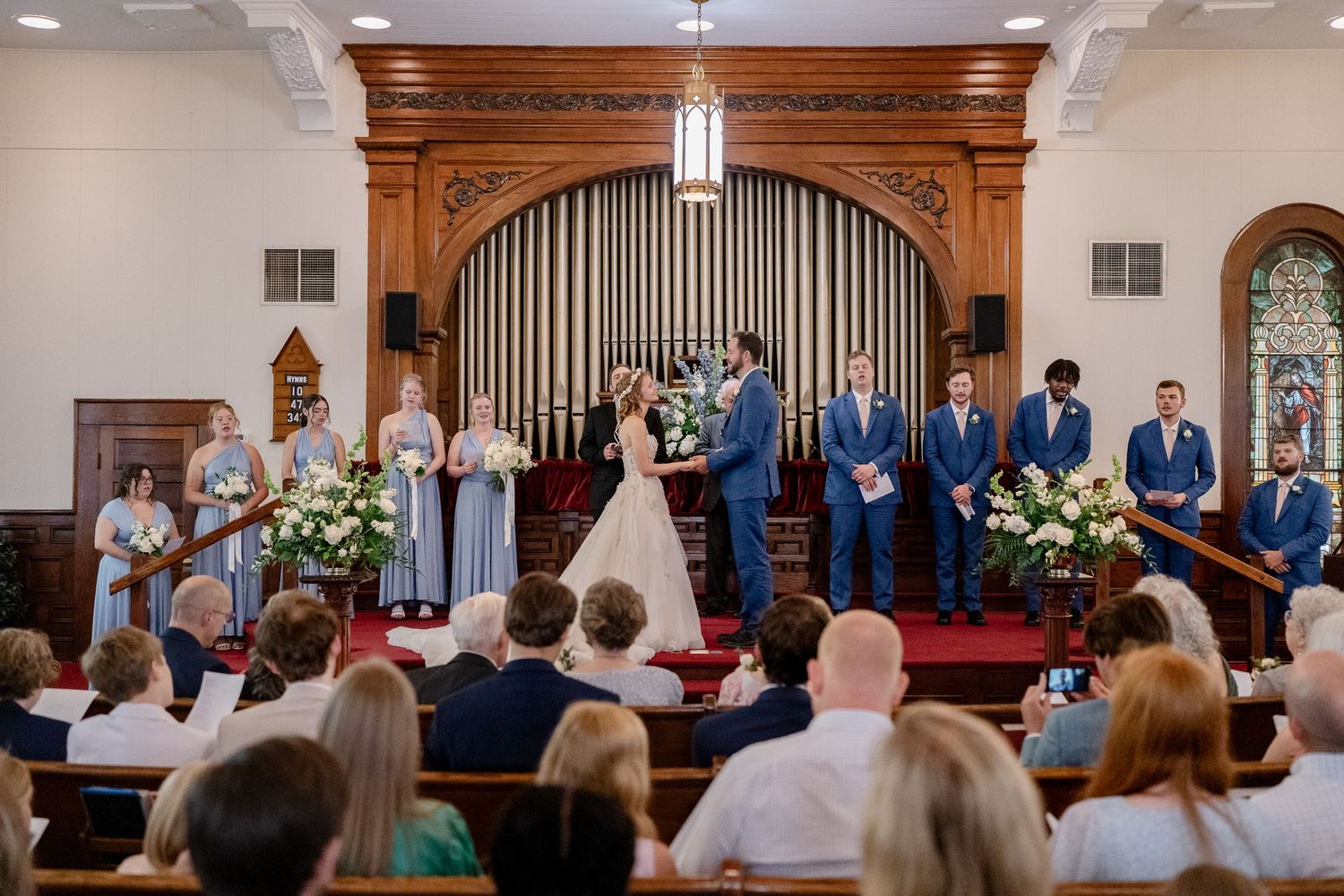 Wide view of a church ceremony with wooden architectural details and pipe organ.