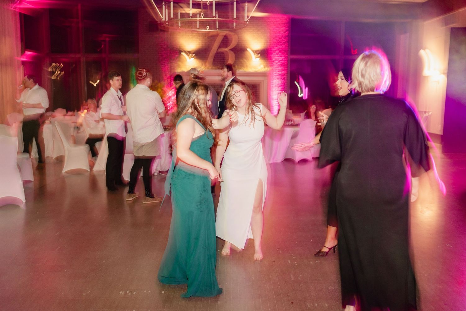 People dancing at a wedding reception under pink and purple lighting in an elegant venue.