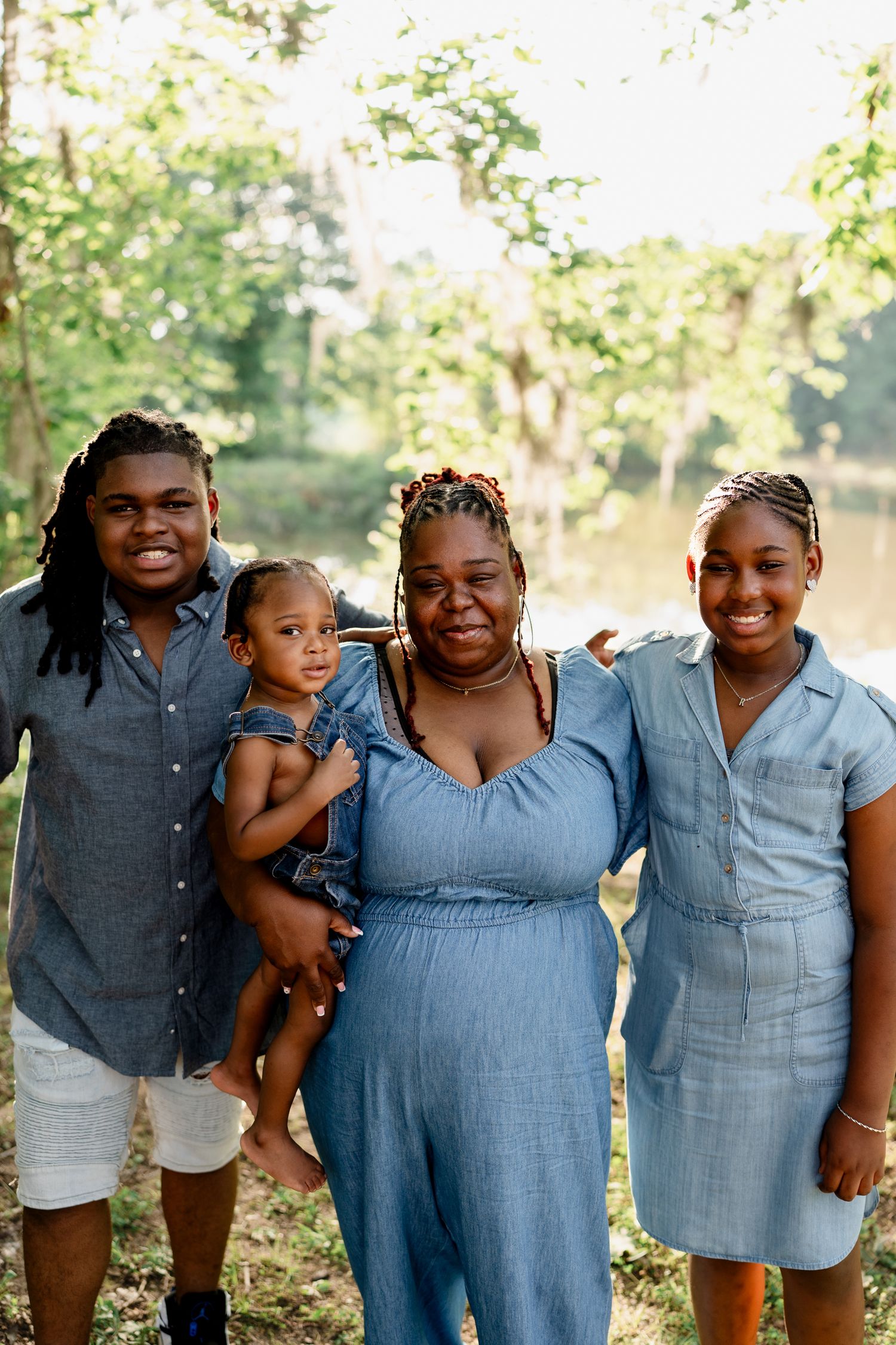 Happy family members pose together in complementary blue outfits during a sunny outdoor photo shoot.
