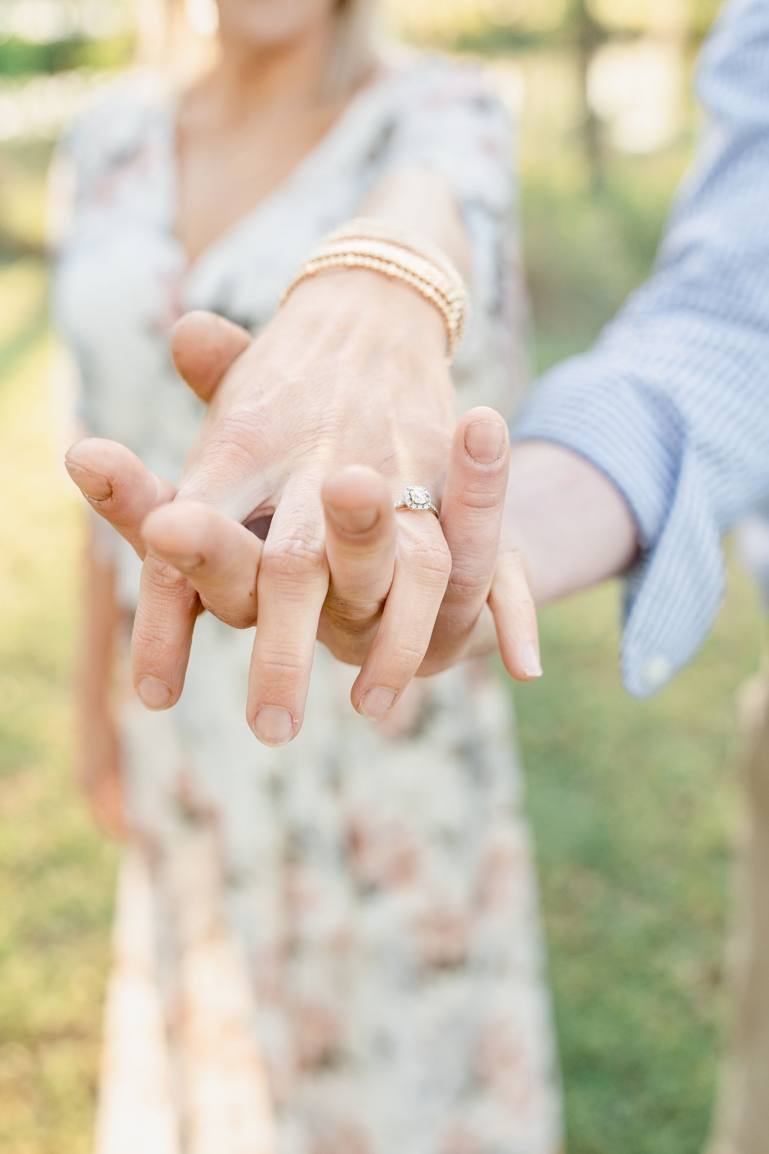 Close-up of hands with an engagement ring and pearl bracelet in natural lighting.