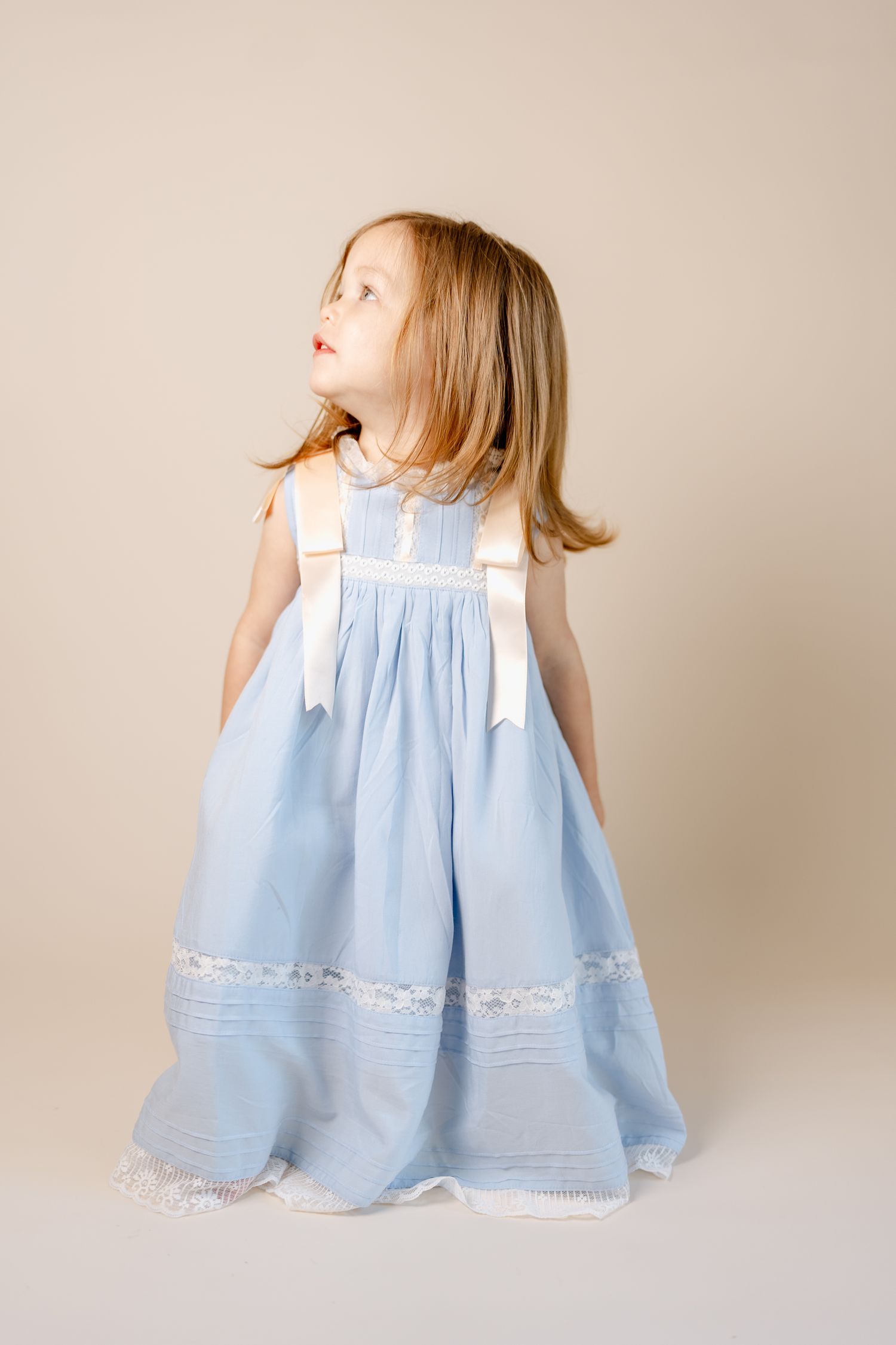 A sweet light blue dress with white lace trim is twirling in a simple studio against a beige background.