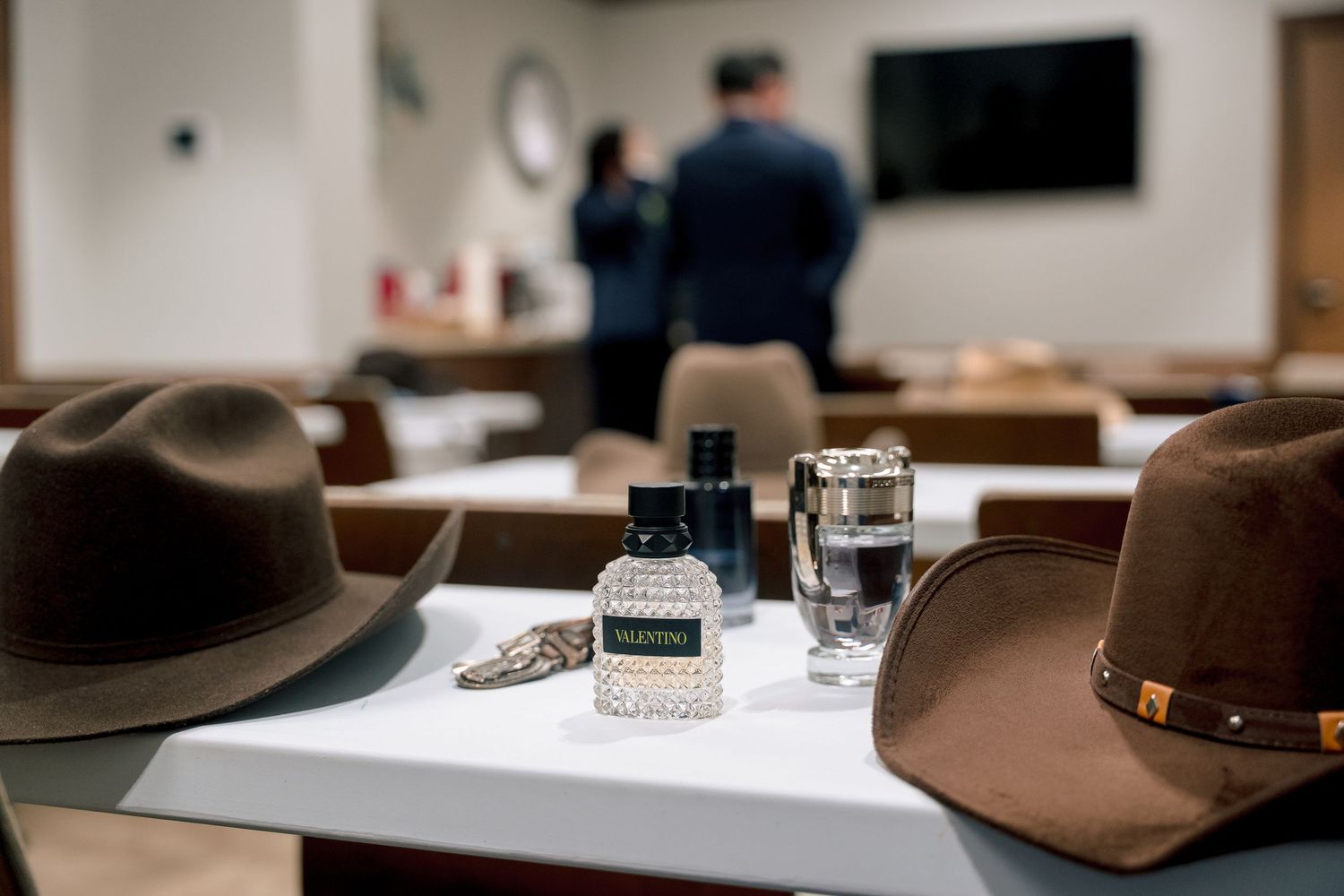 A brown fedora hat sits next to a glass bottle on a wooden table in a dimly lit room.
