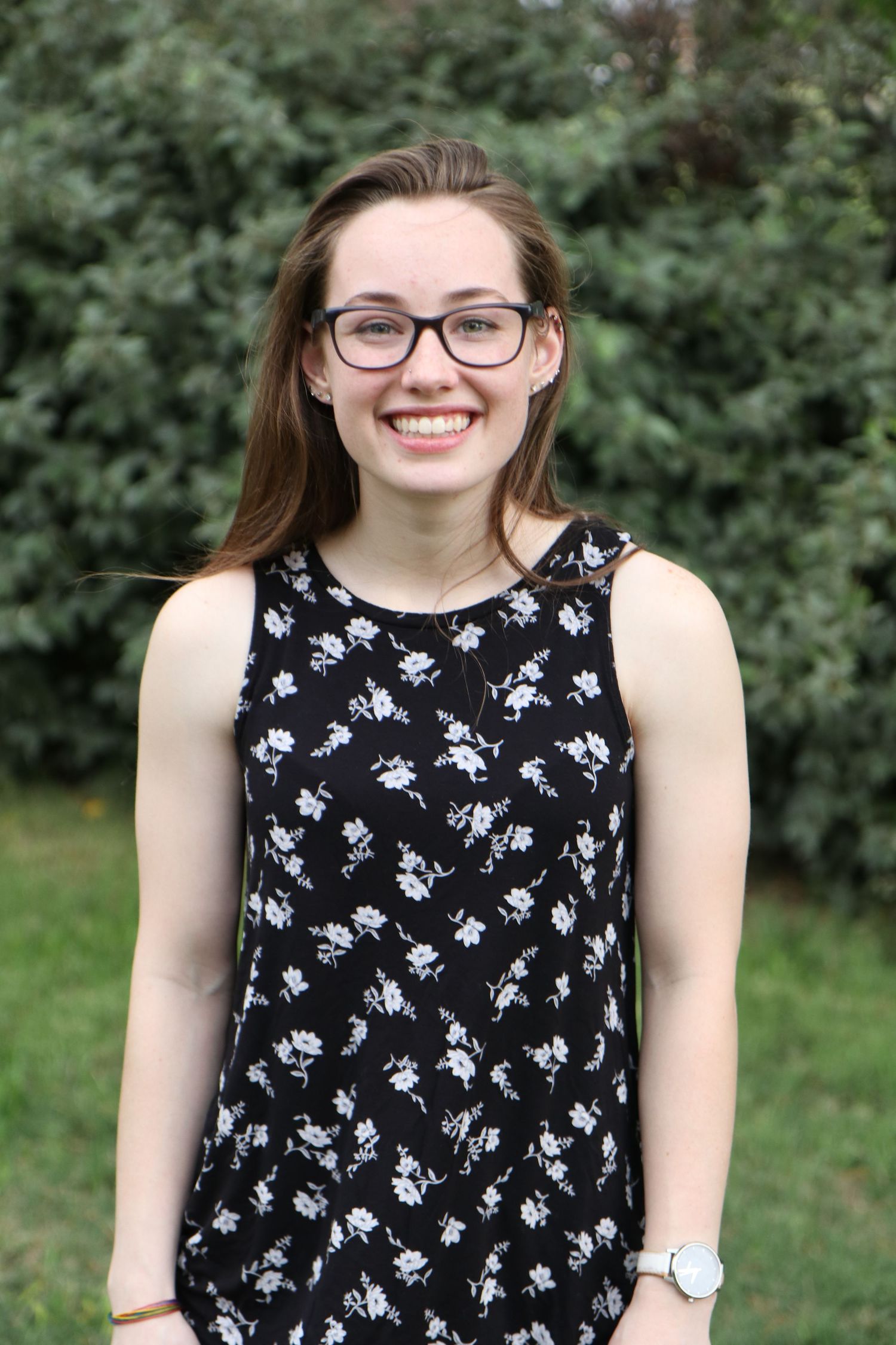 A cheerful portrait taken outdoors wearing a black and white floral sleeveless top.