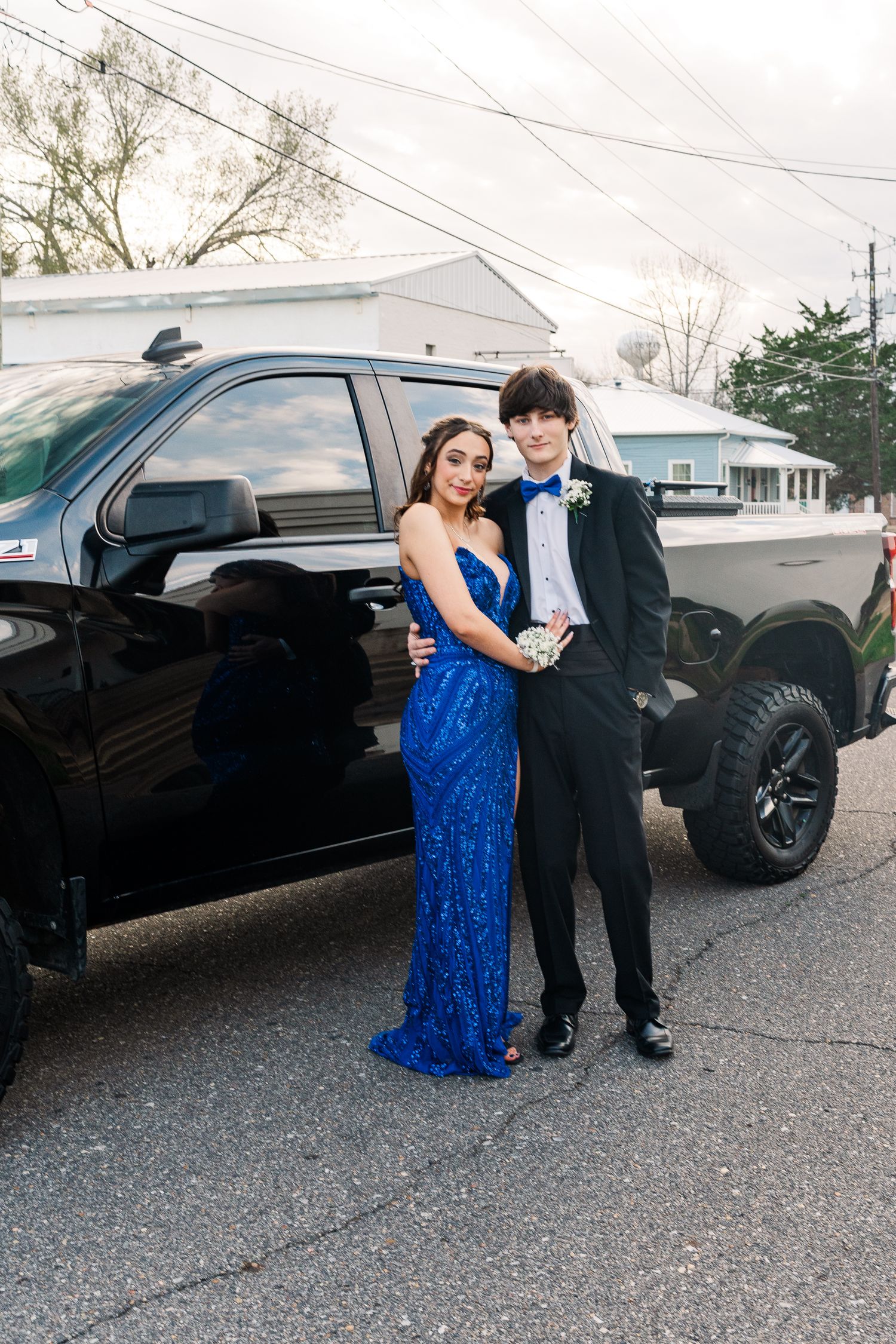 A couple stands near a black pickup truck in formal attire for photos.