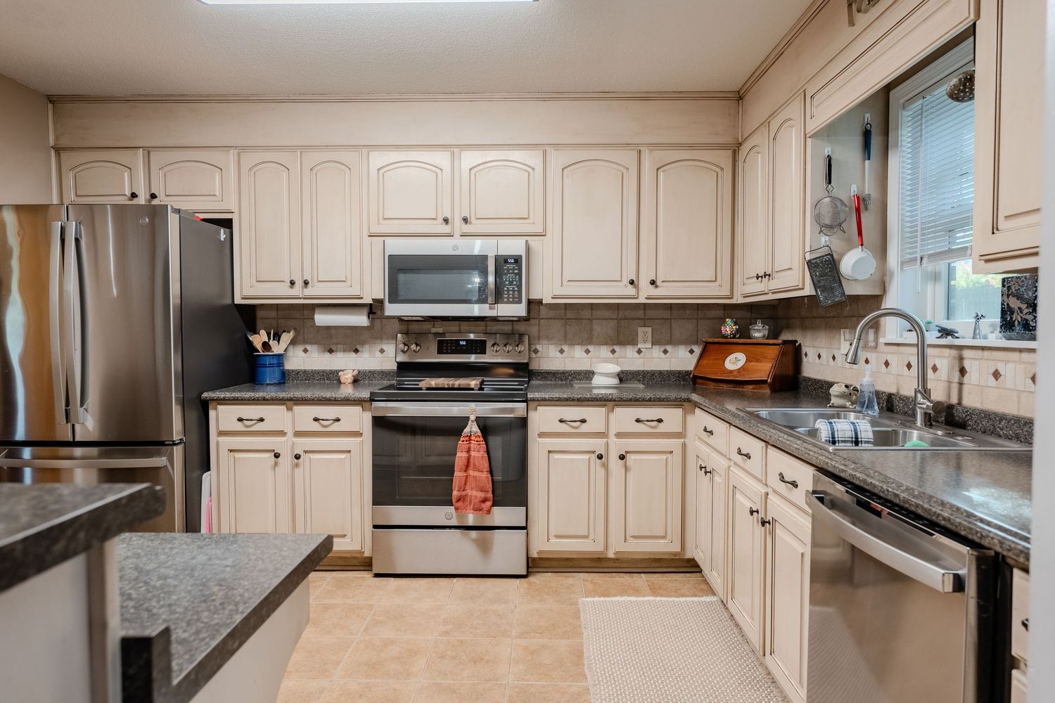 Modern white kitchen with stainless steel appliances, granite countertops, and ornate cabinetry in a bright open layout.