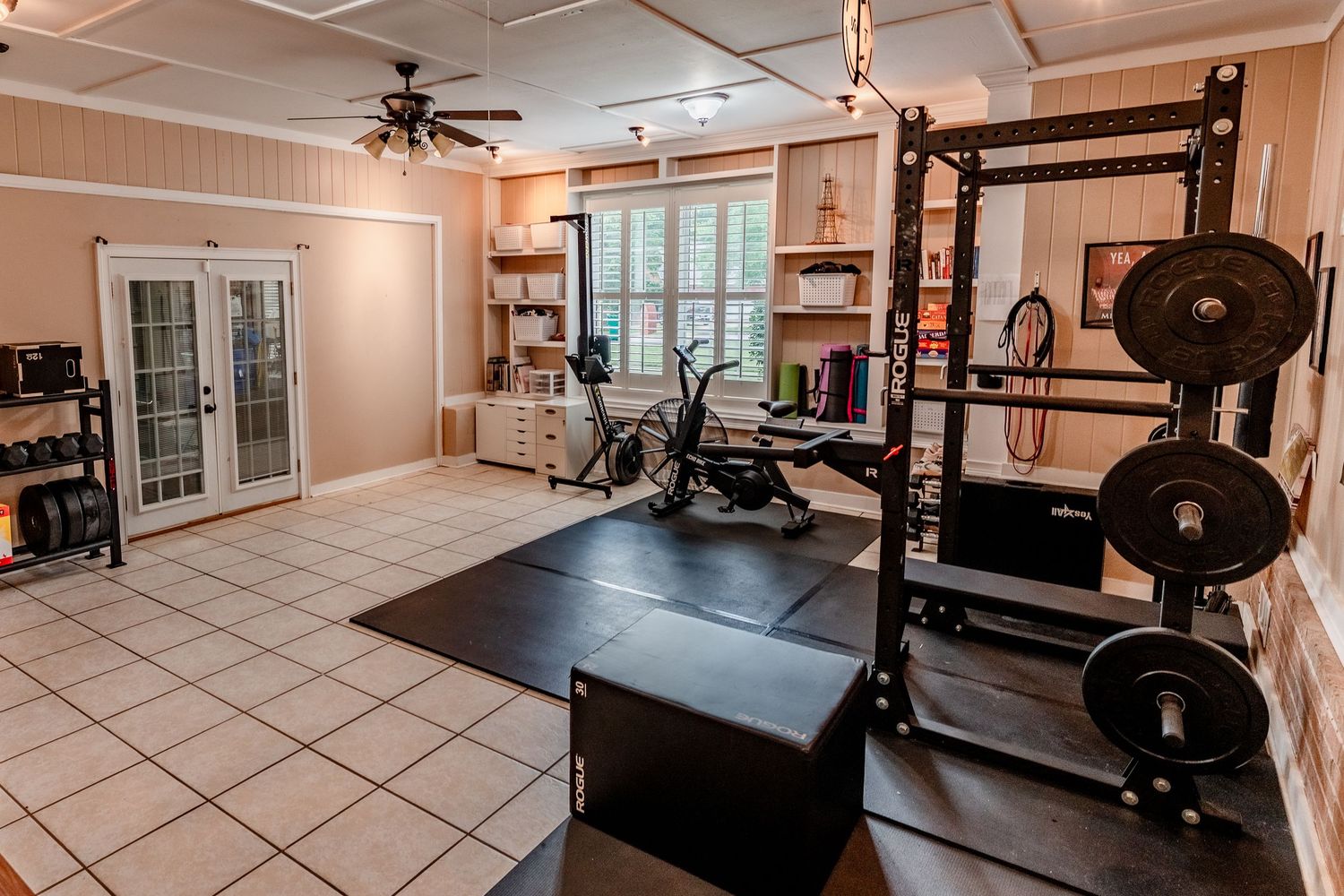 Modern home gym setup with dark equipment, mirrors, and tile flooring in a well-lit space.