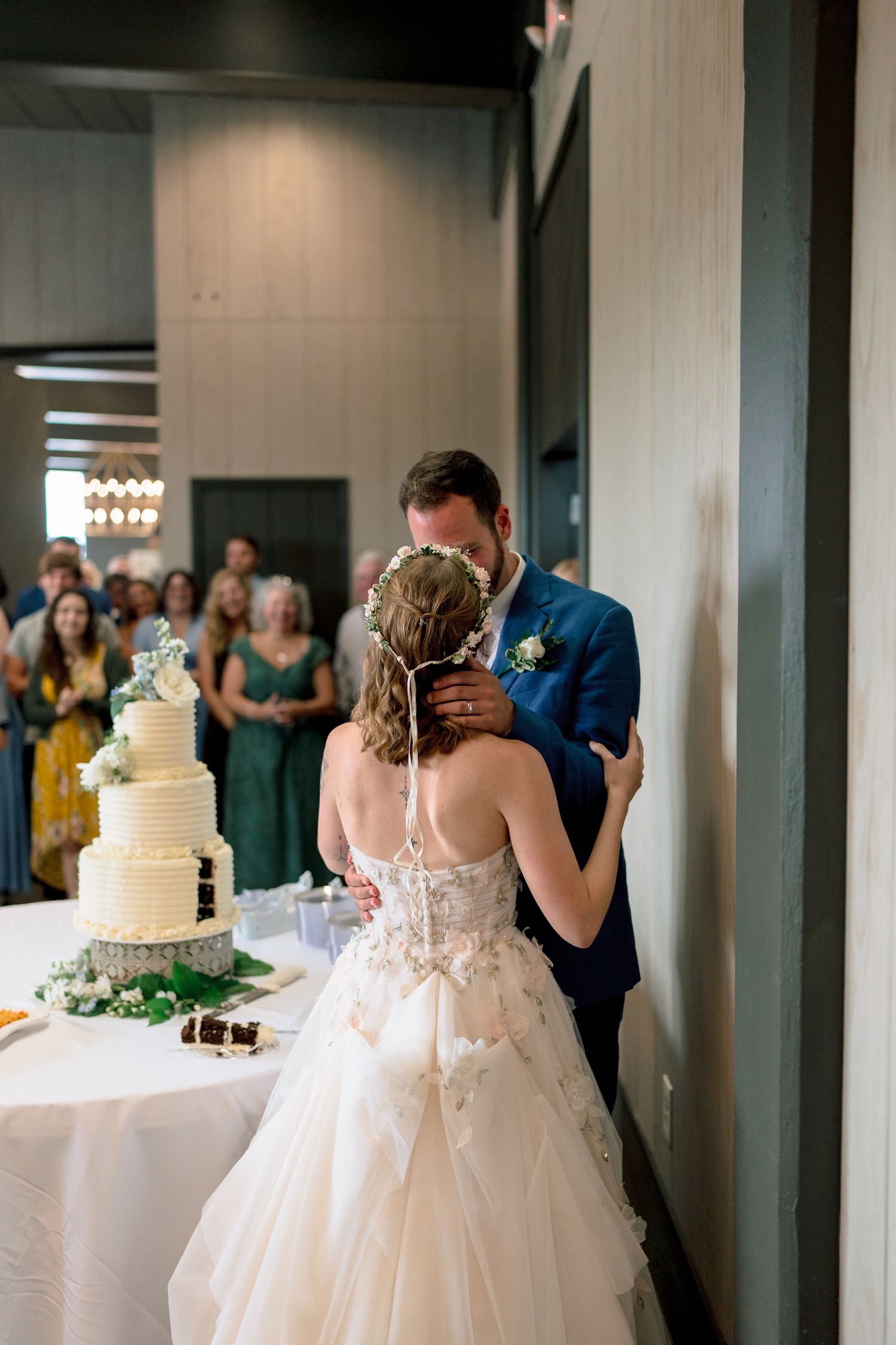 Bride and groom share a kiss while cutting their white wedding cake at their elegant reception.