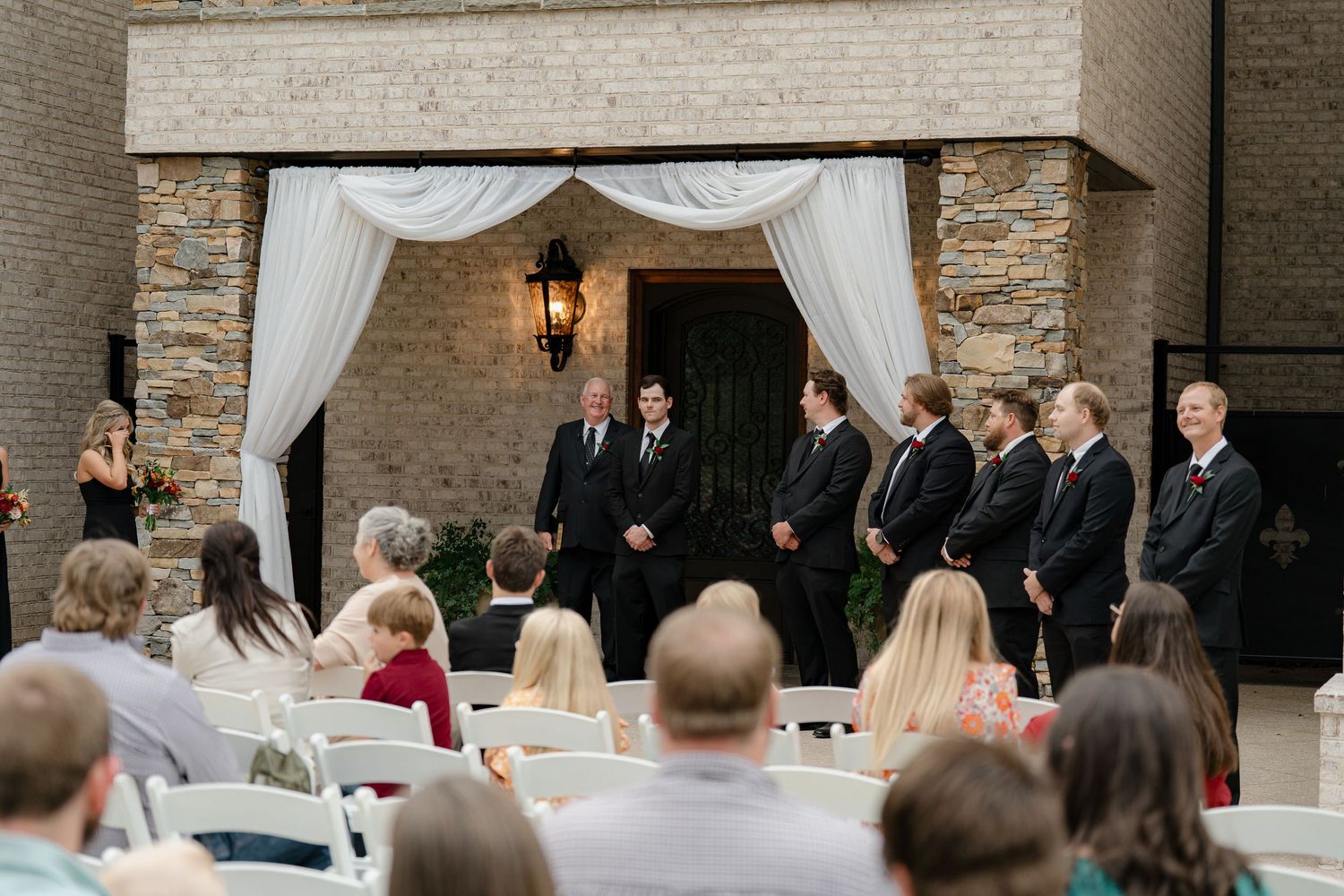 Wedding guests seated outdoors at a rustic brick venue during an evening ceremony.