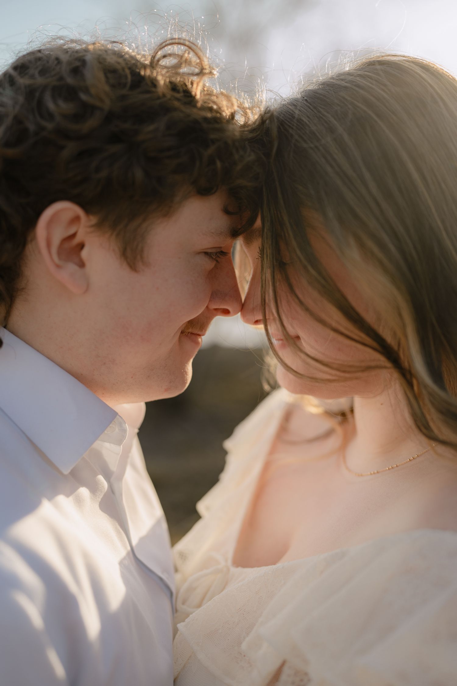 Couple leaning foreheads together in golden sunlight in a tender romantic moment.