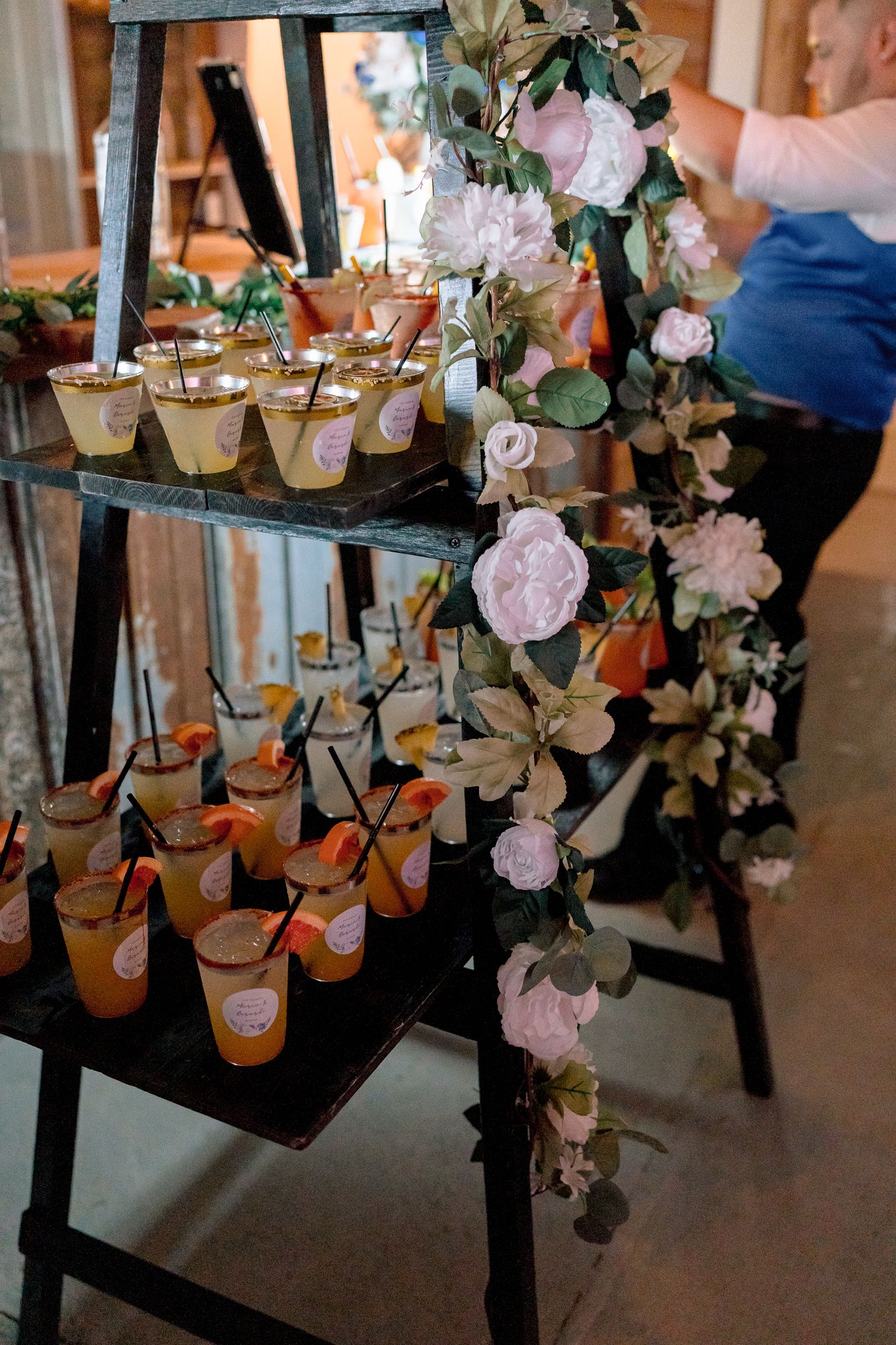 Decorative display of small bottles with pink floral accents hanging from a black ladder shelf.