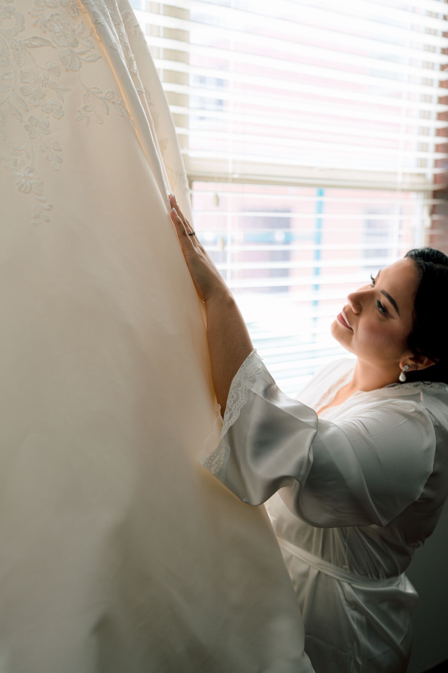 Person in gray shirt leaning back against wall with sunlight streaming through window blinds.