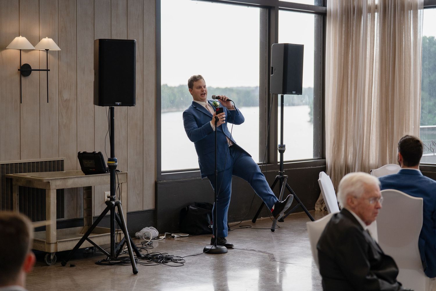 Professional speaker presenting to an audience in a modern meeting room with wood paneled walls and large windows.