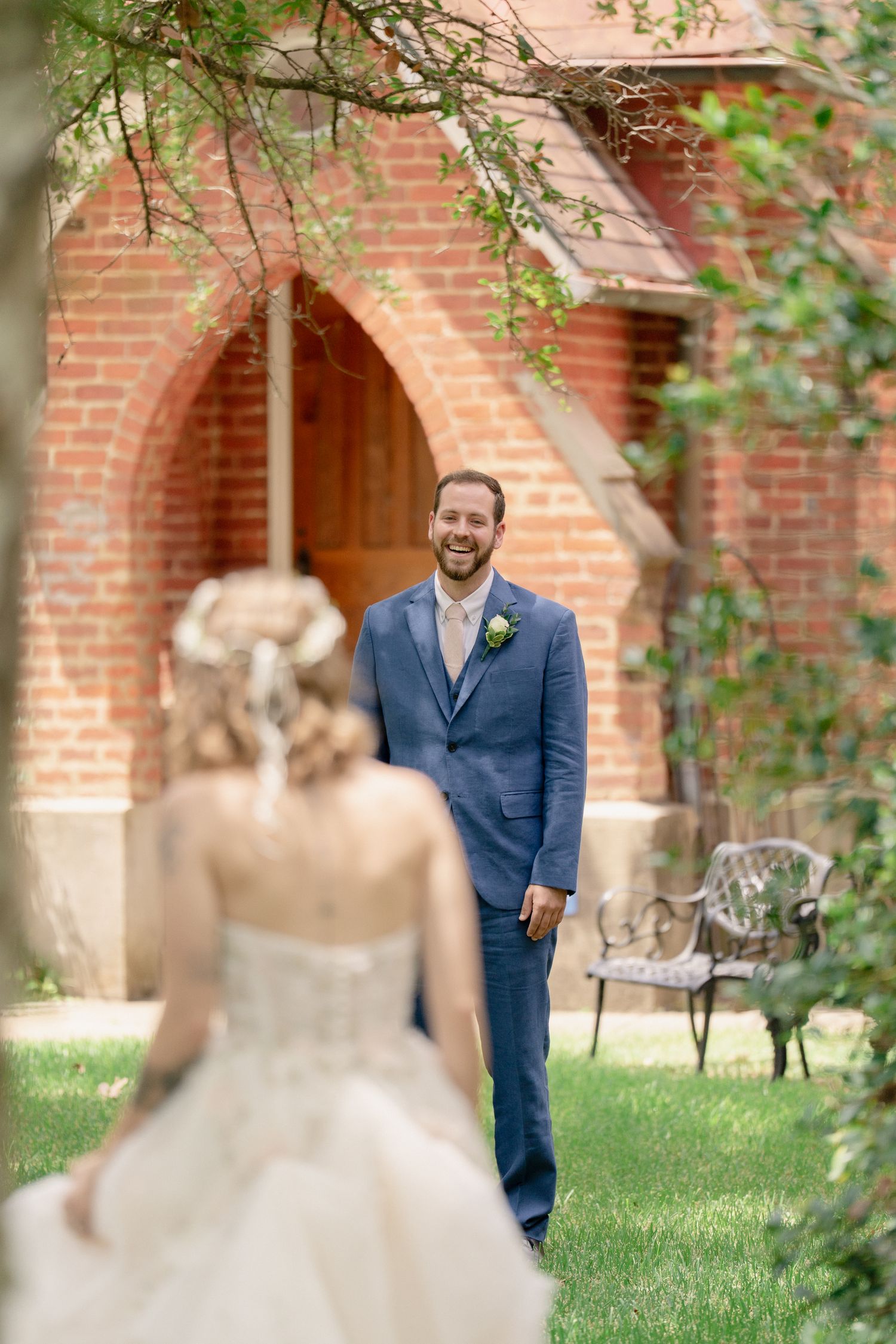 A first look moment between a bride and groom in a garden courtyard with red brick walls and greenery.