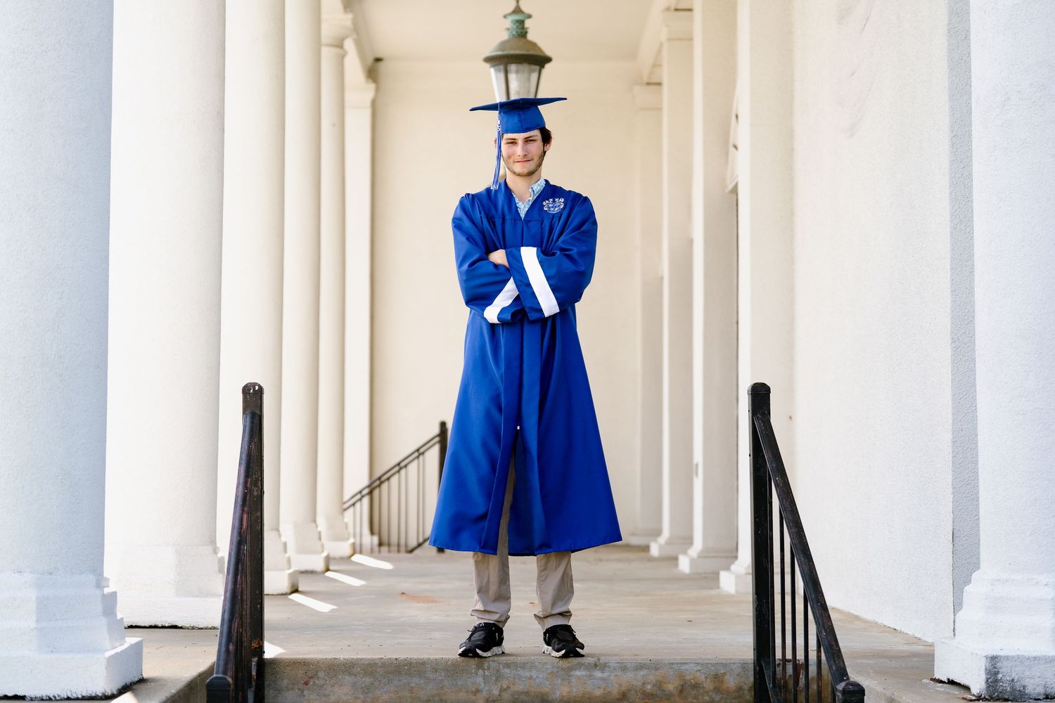 Graduate in blue cap and gown poses confidently between white columns.