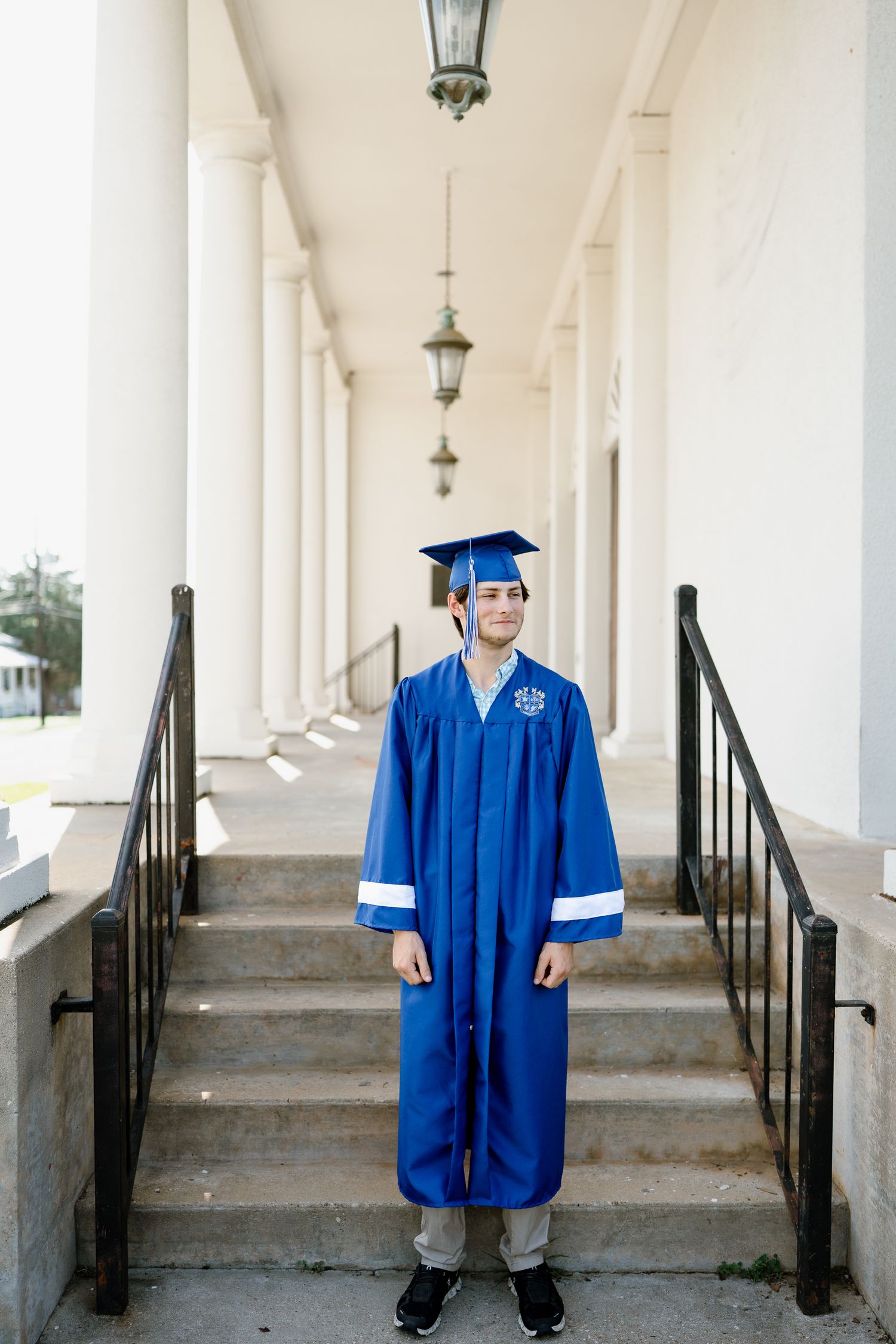Graduate in blue regalia stands on steps between classical white columns.