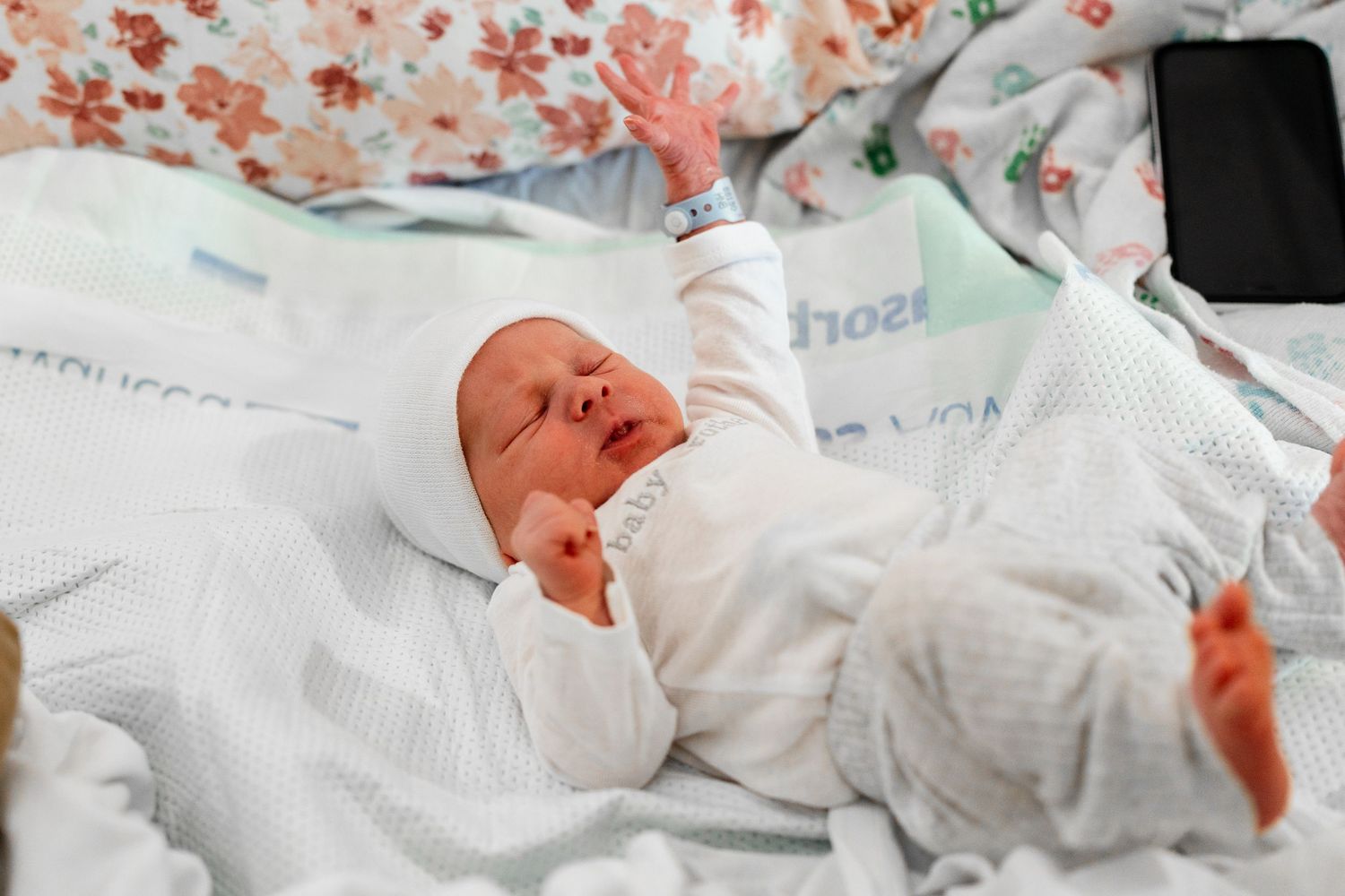 Newborn baby swaddled in white blanket lying on floral patterned bedding.