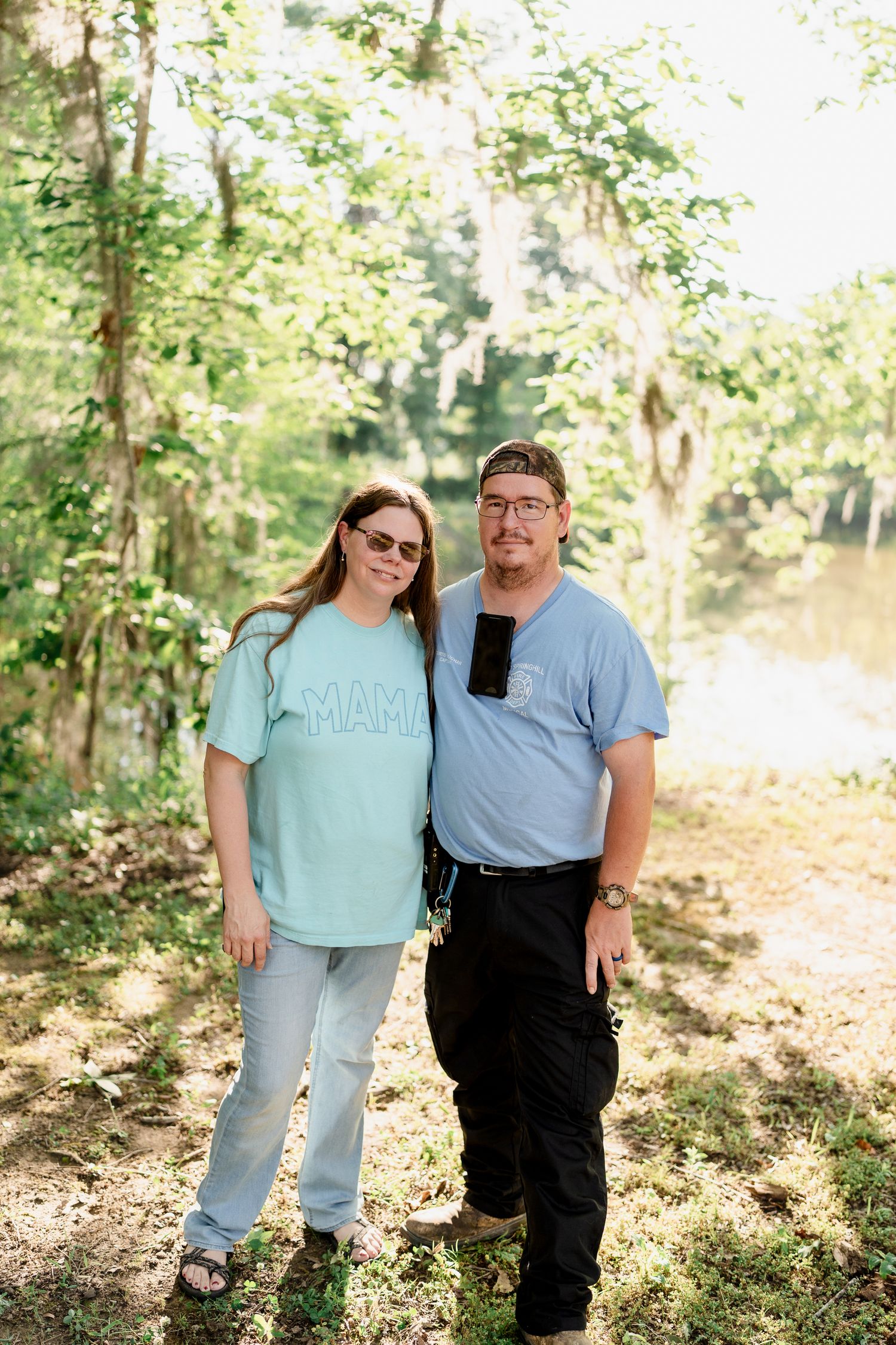 A couple in coordinating blue outfits poses together for photos in a wooded outdoor setting.