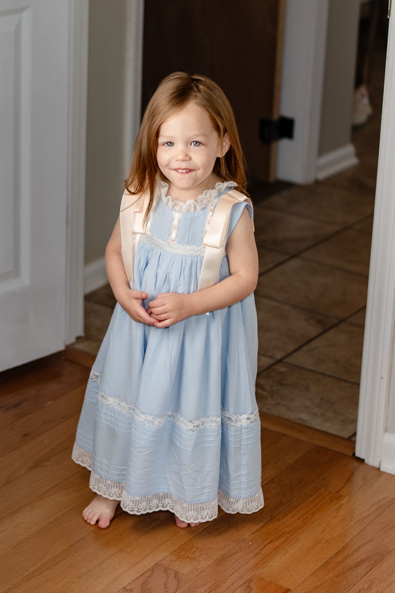 Child wearing vintage-style blue and white dress with lace trim on hardwood floor.