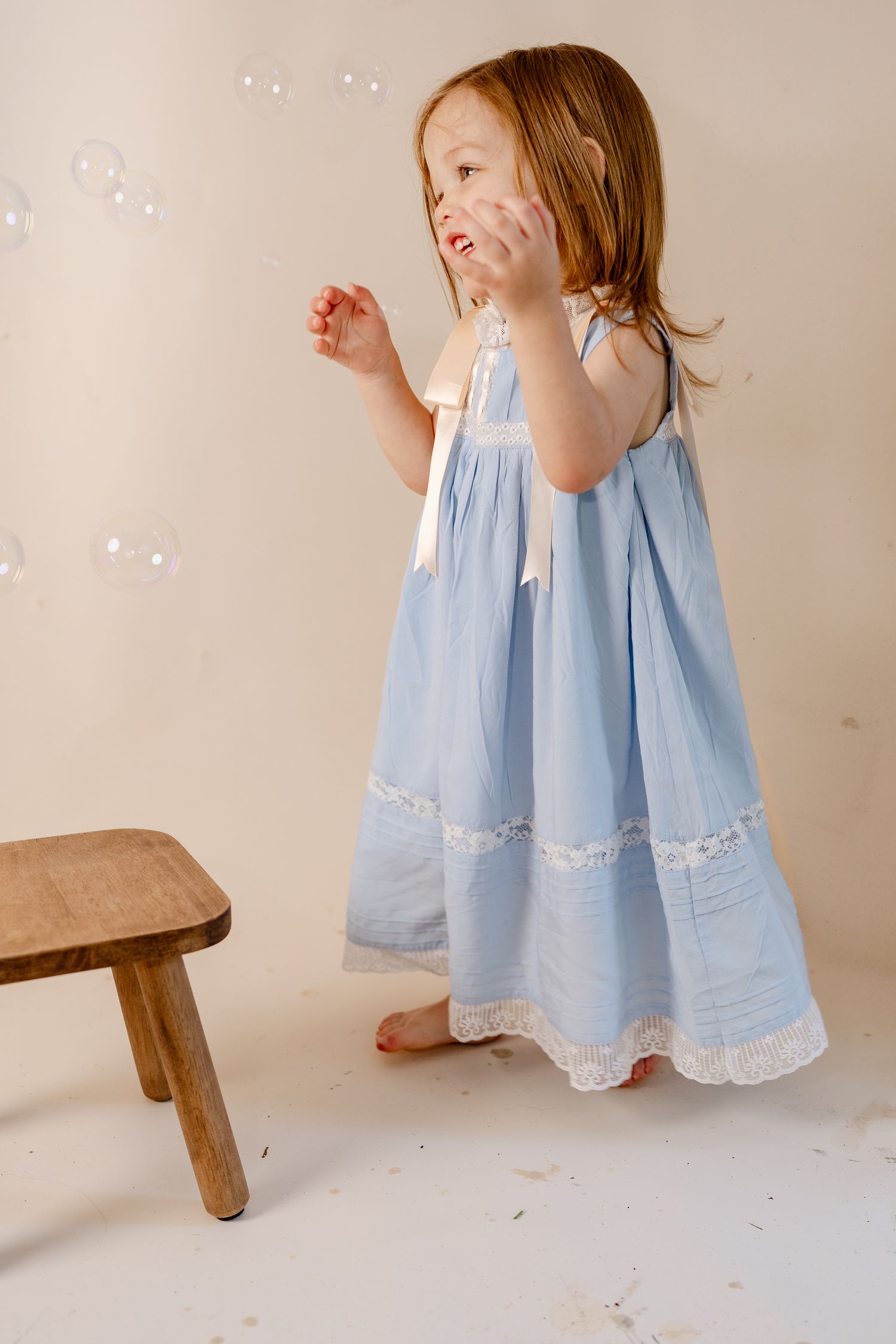 A light blue dress with lace trim flows against a neutral studio backdrop.