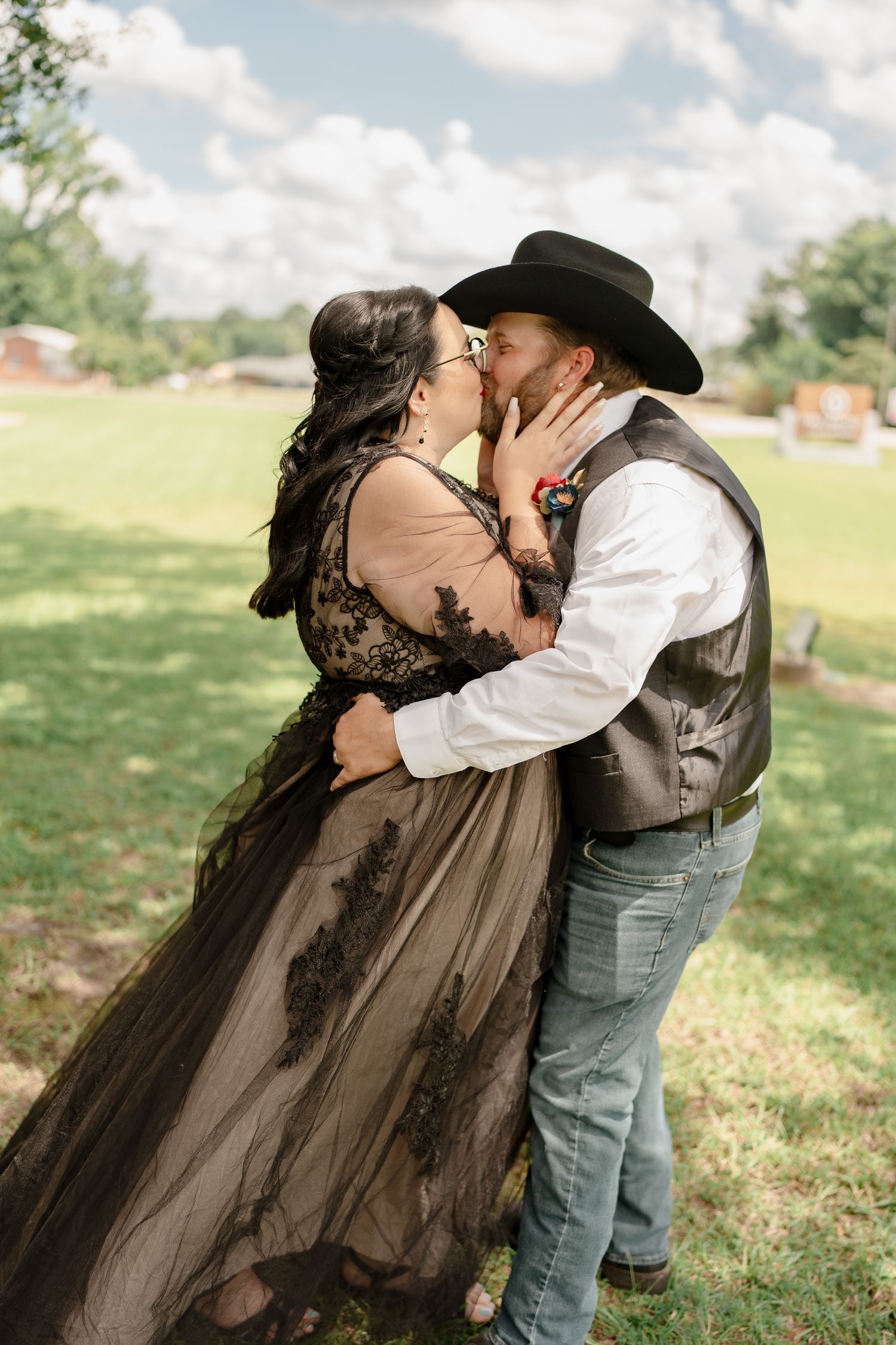 A romantic moment captured outdoors with a couple in western attire, featuring a black tulle dress and cowboy hat.