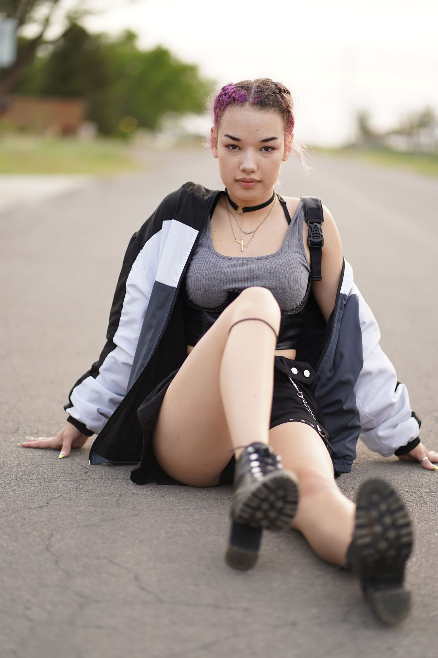 Person in street fashion with combat boots and bomber jacket poses on asphalt road.