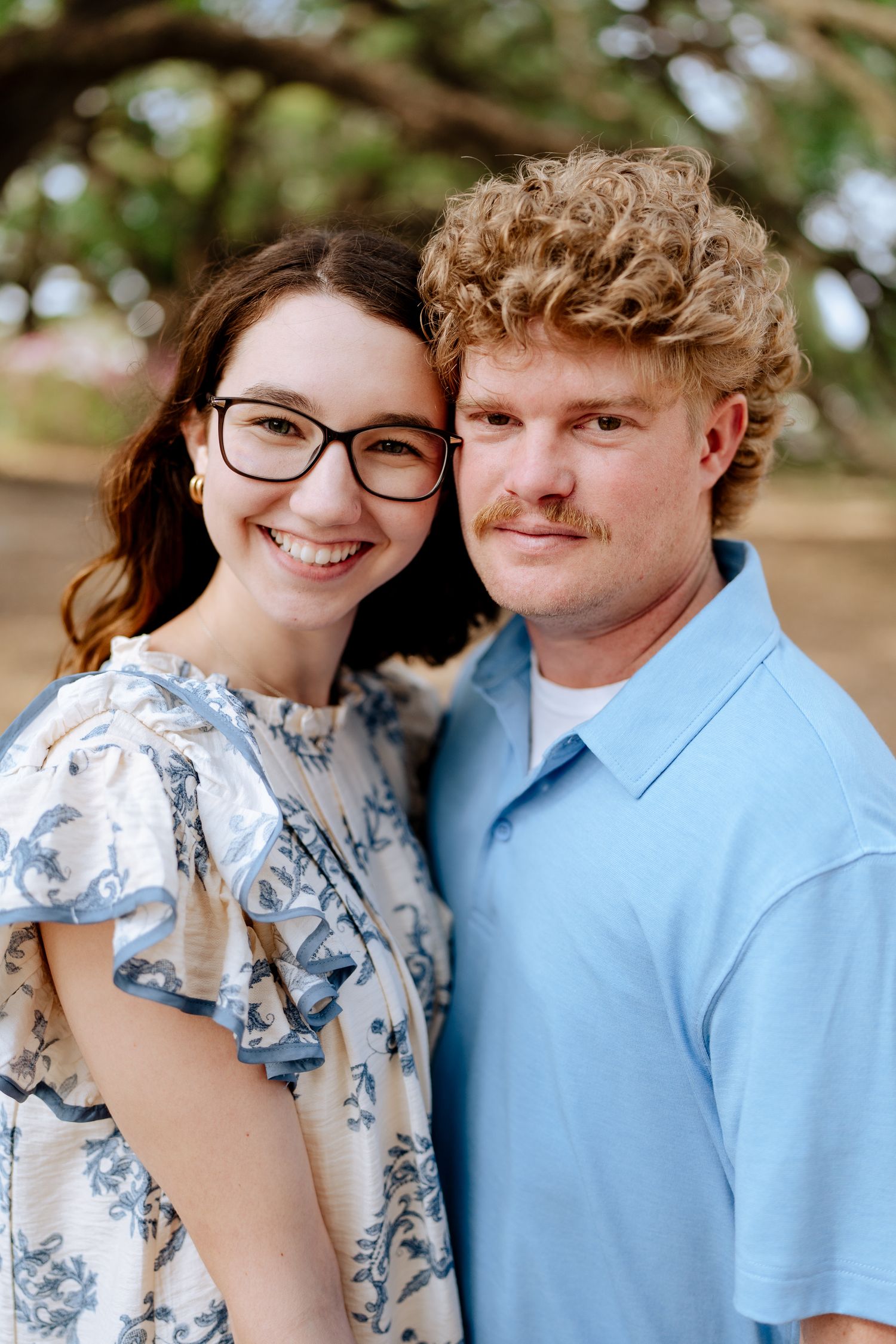 Couple in coordinating blue outfits share intimate moments under oak trees.