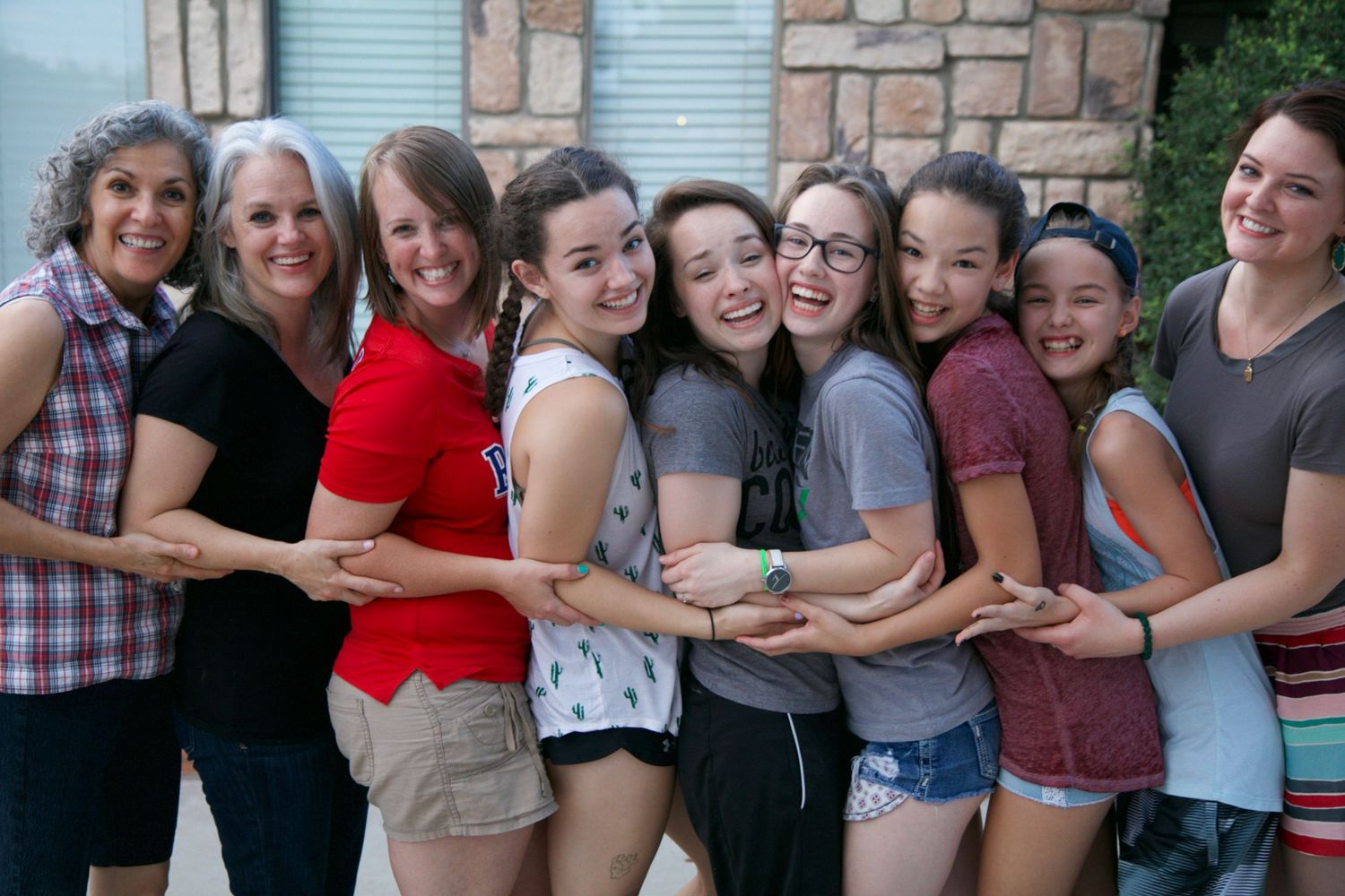 A group of friends stand close together in a row, sharing joyful expressions.