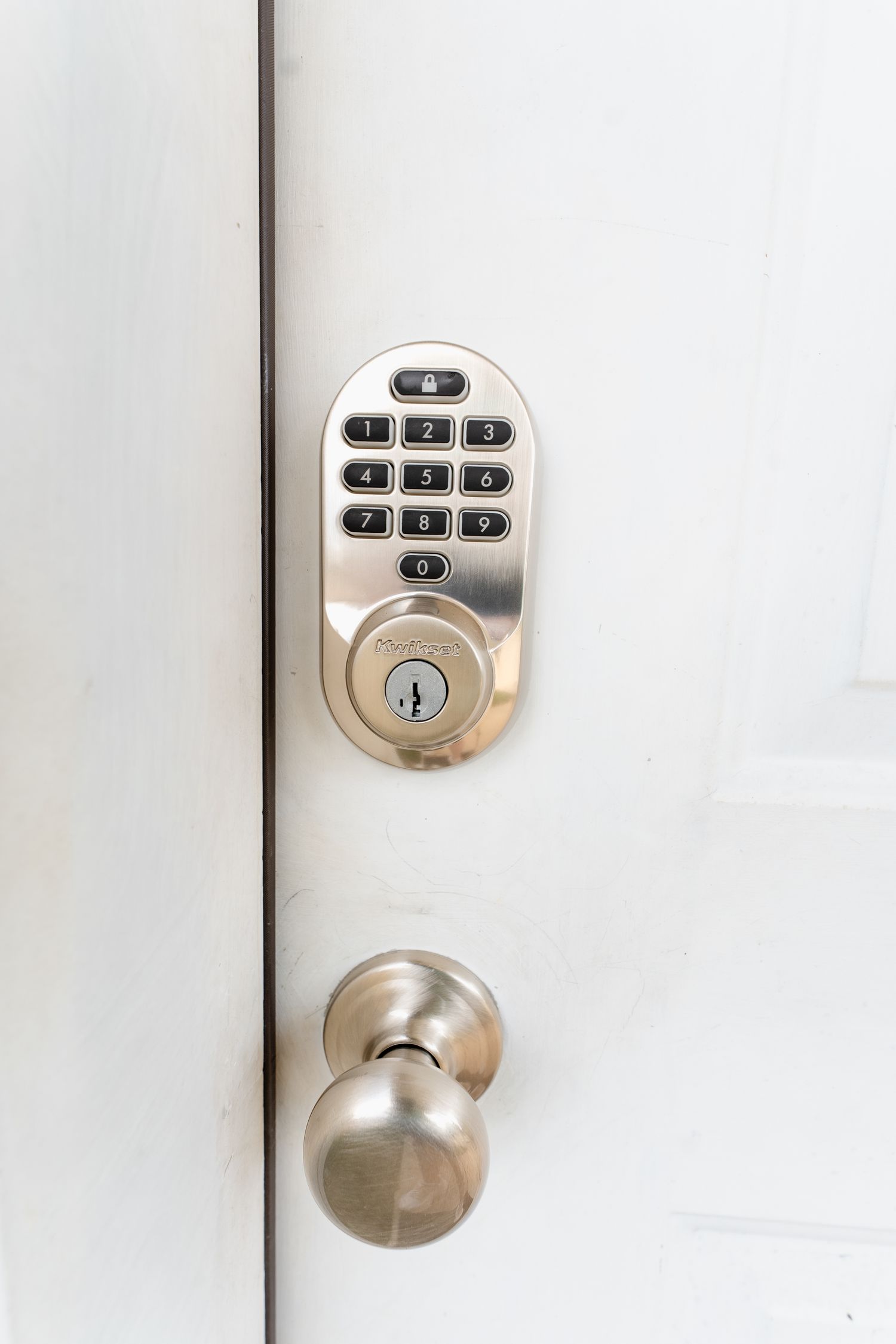 Digital keypad door lock with brushed silver finish and round doorknob mounted on white door.