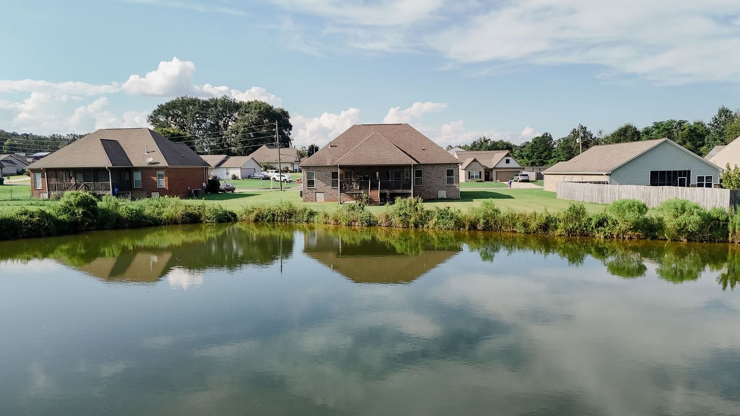 A panoramic view of lakefront houses with calm water reflections and cloudy skies stretching across the horizon.