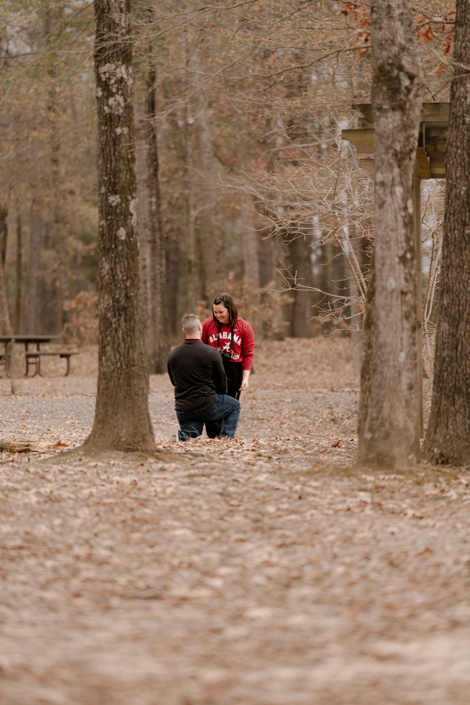 A couple walking through a forest path covered in fallen autumn leaves on a romantic afternoon.
