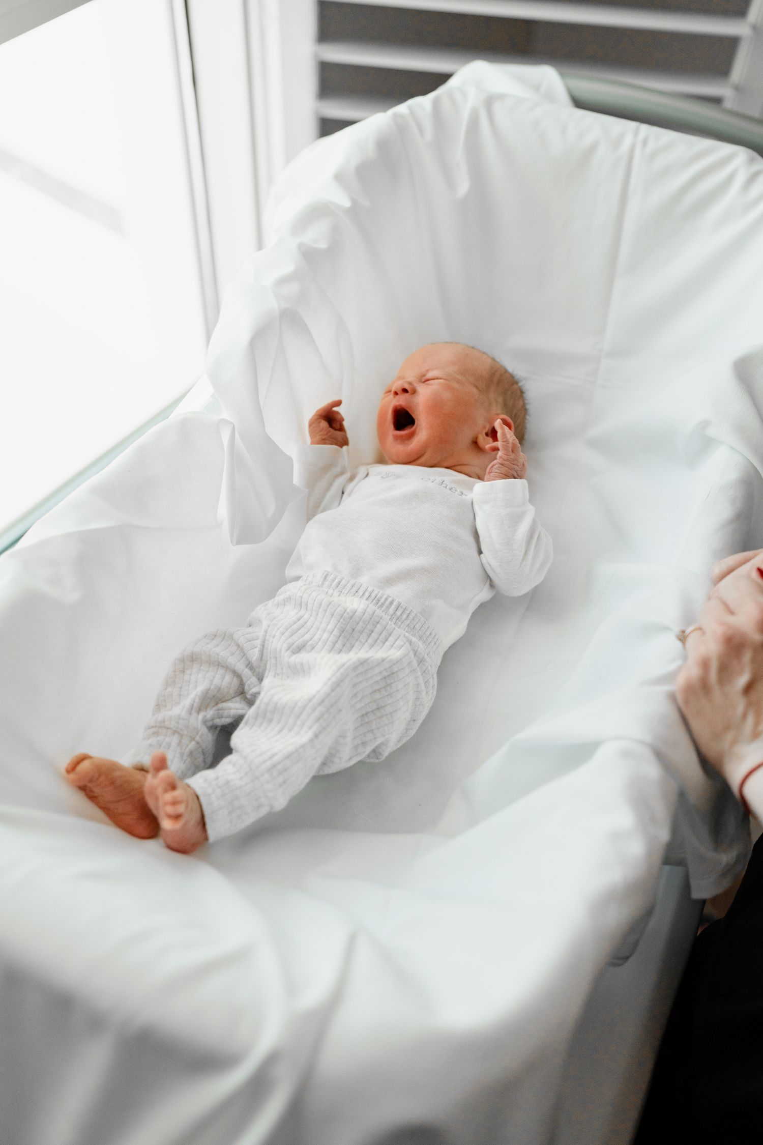 Baby in white outfit resting peacefully on white blankets in series of photos.